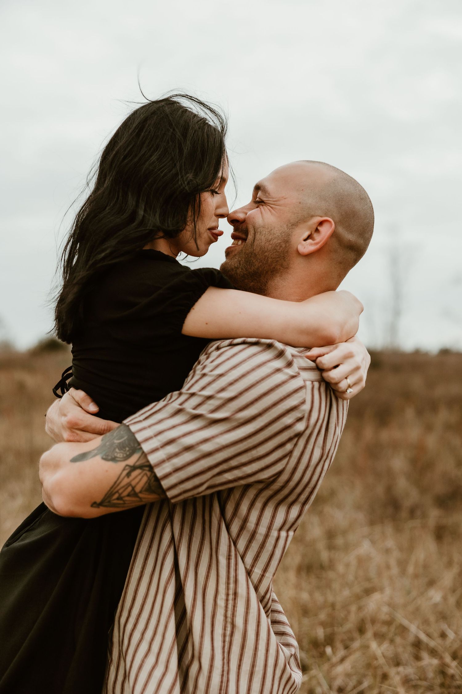 A romantic couple embraces lovingly in a field during golden hour, creating an intimate outdoor portrait.