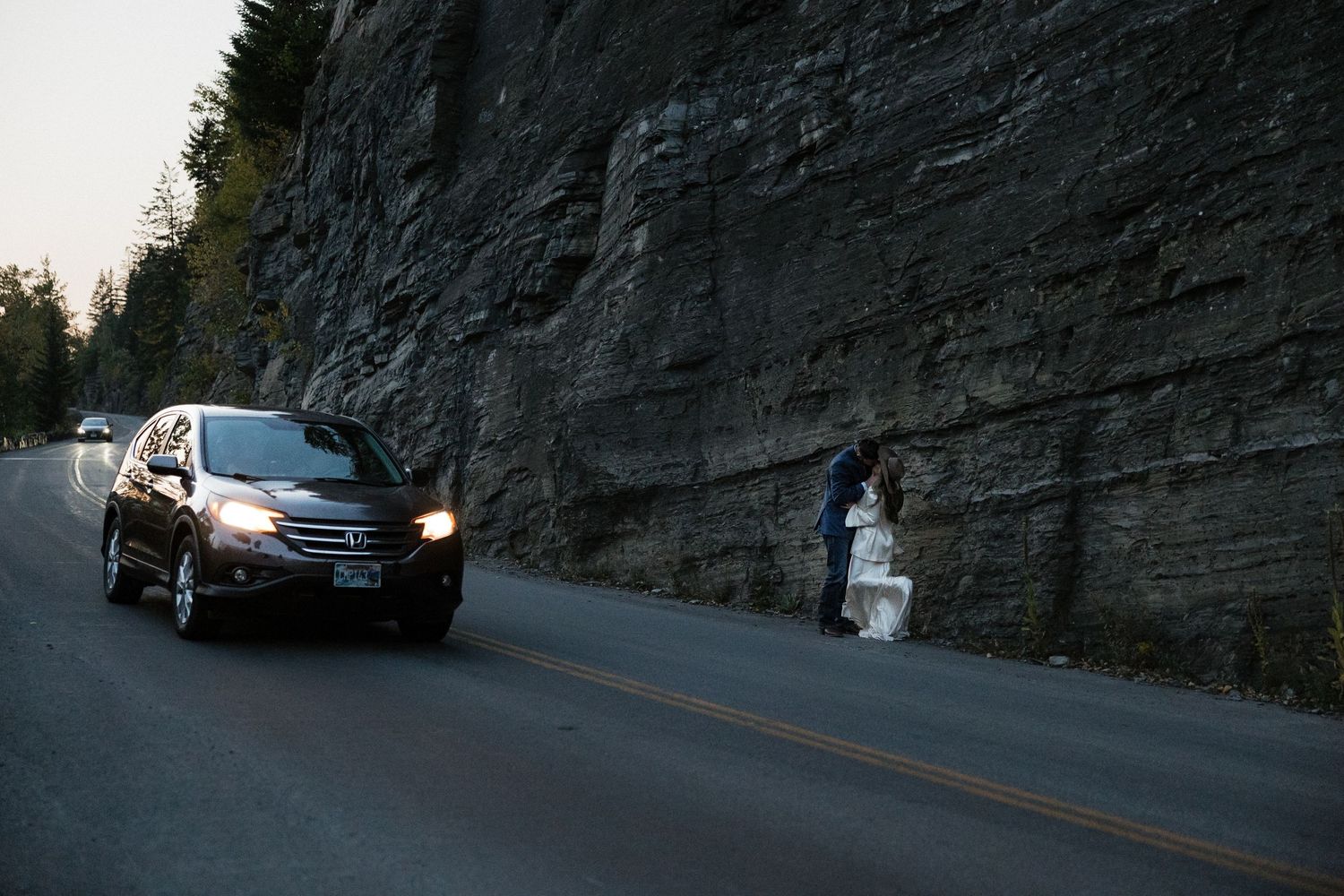 A scenic mountain road cuts through tall rocky cliffs during golden hour.