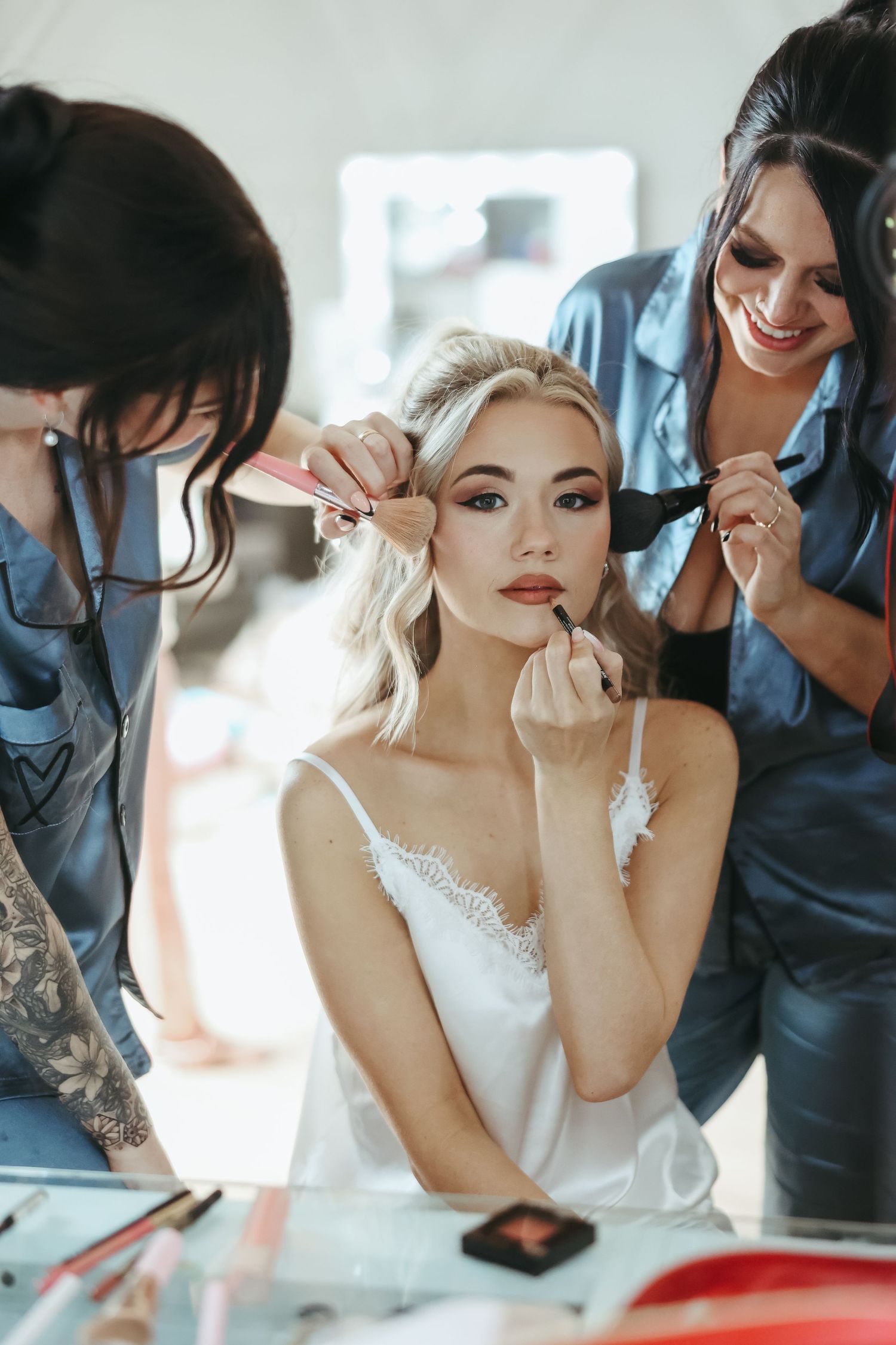 Professional makeup artists and hairstylists prepare a bride in a delicate white lace slip for her wedding day.
