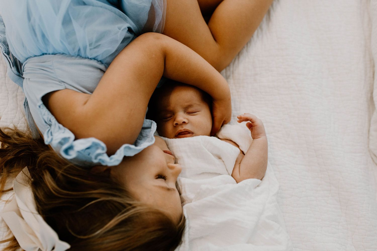 A parent and young baby resting together in white bedding.