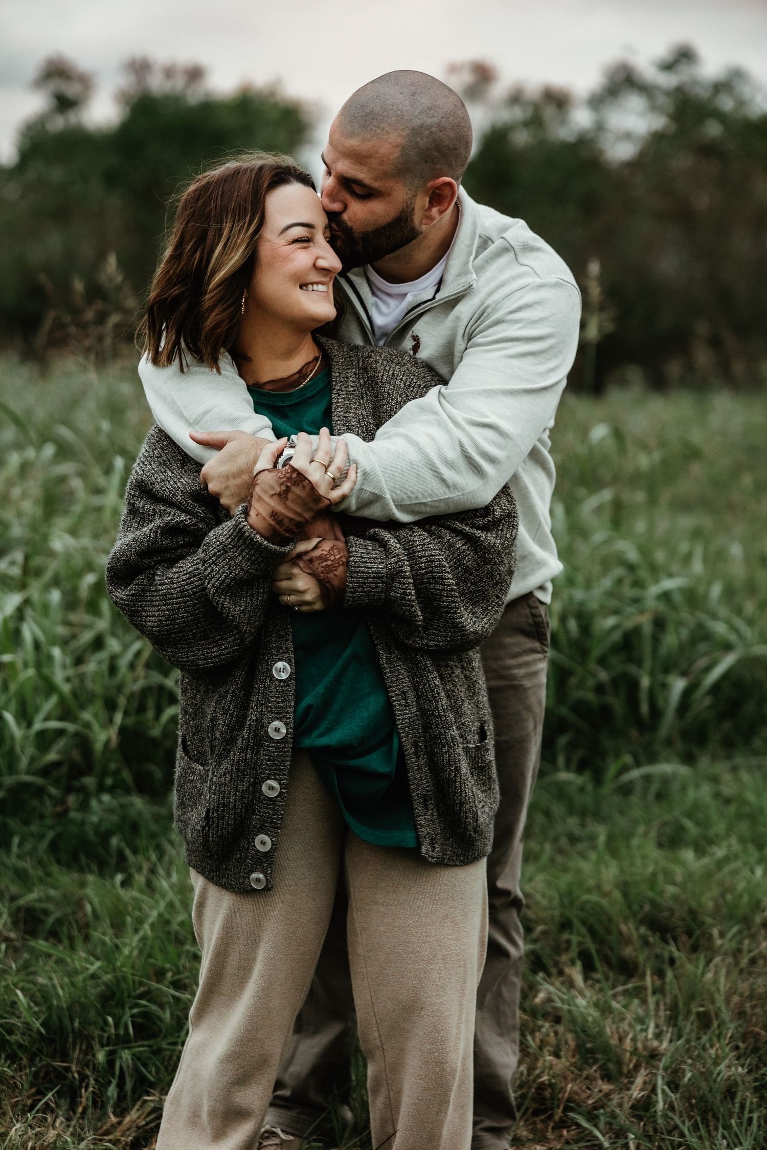 A couple embraces in a field of tall grass during an intimate outdoor photoshoot at sunset.