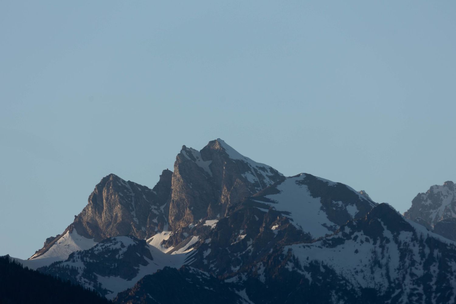 Snow-capped mountain peak with jagged rocky outcrops against a dusky blue sky in the wilderness.
