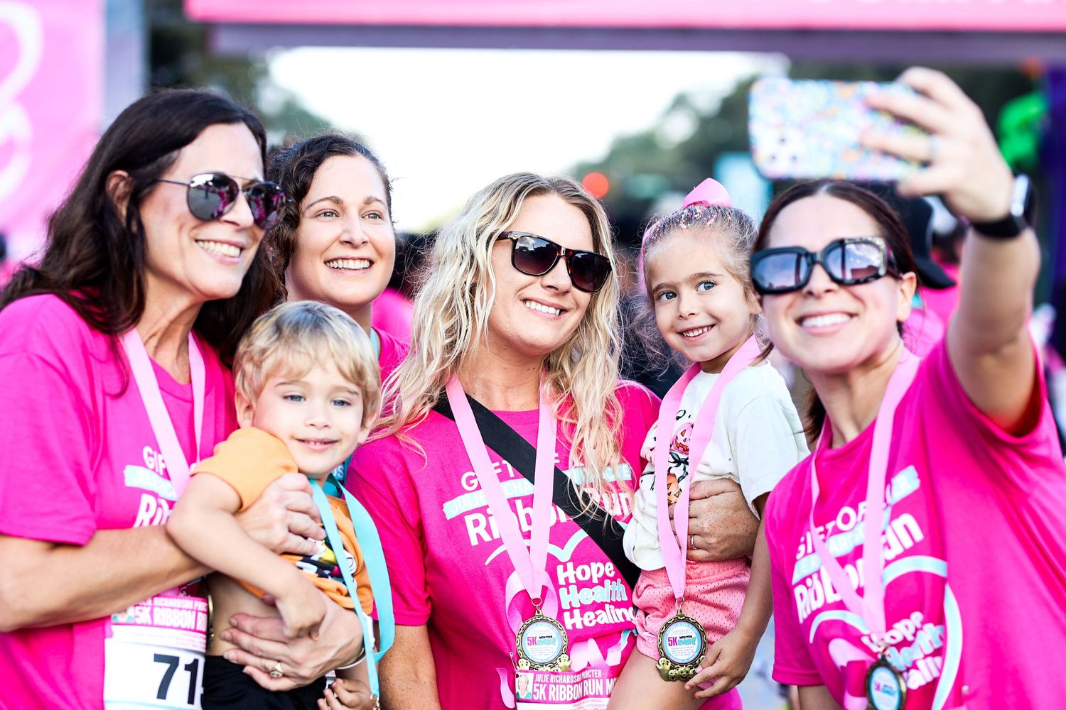 Group of participants in pink shirts taking selfie at breast cancer charity race event.
