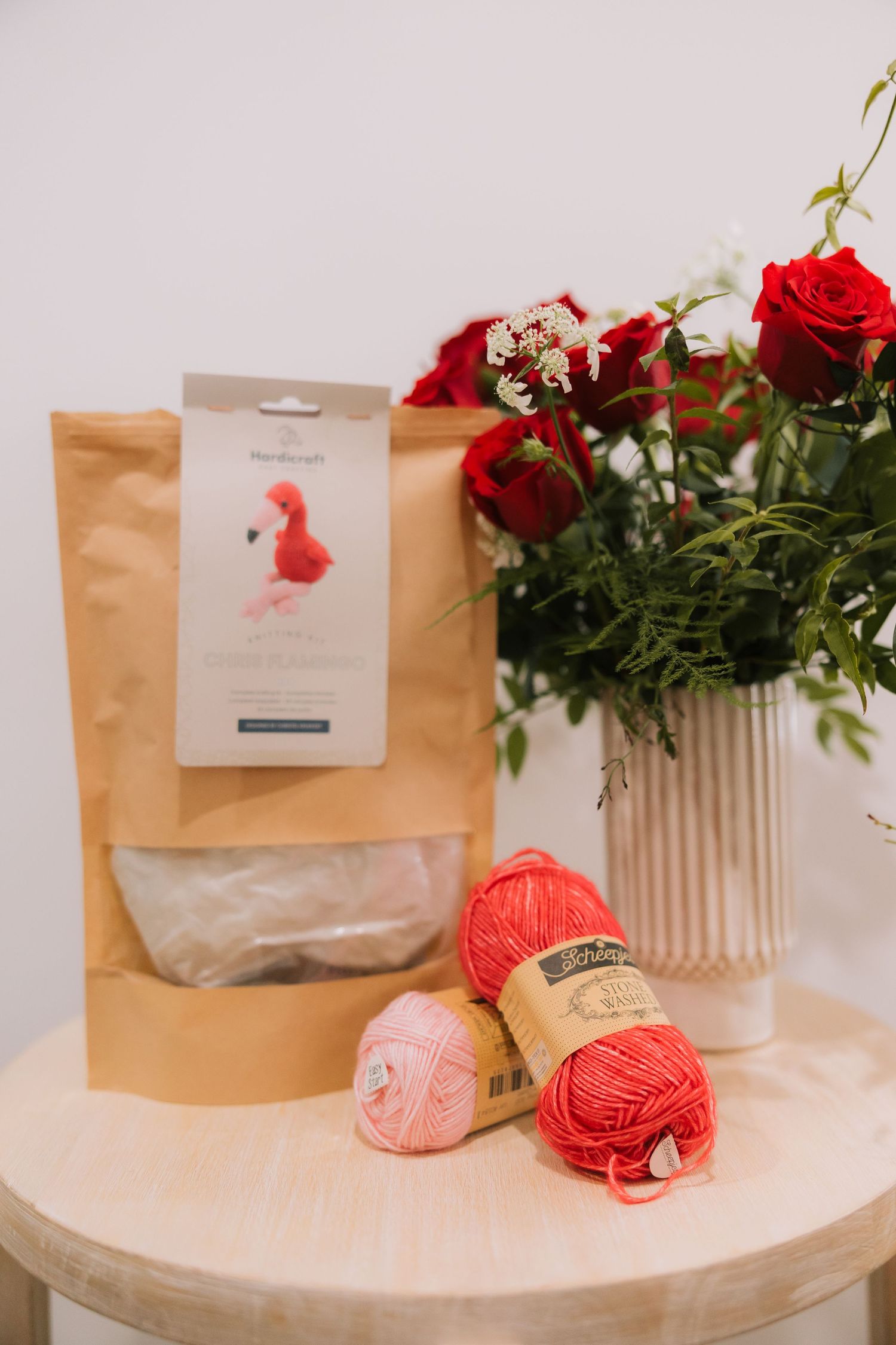 A series of brown paper bags and red yarn balls arranged with red roses on a white round table.