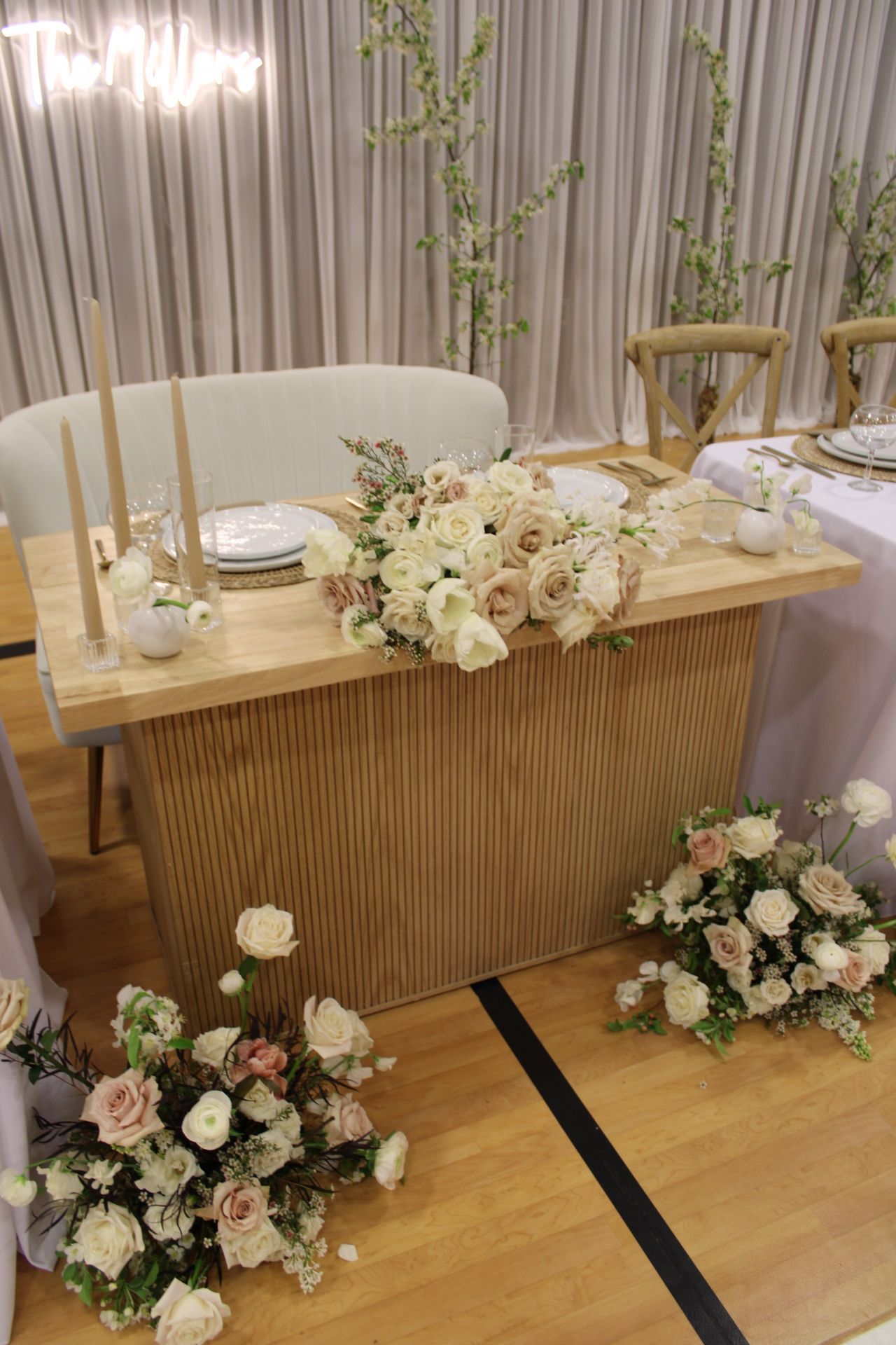 Modern wooden wedding table with blush and white floral arrangements and tall taper candles.