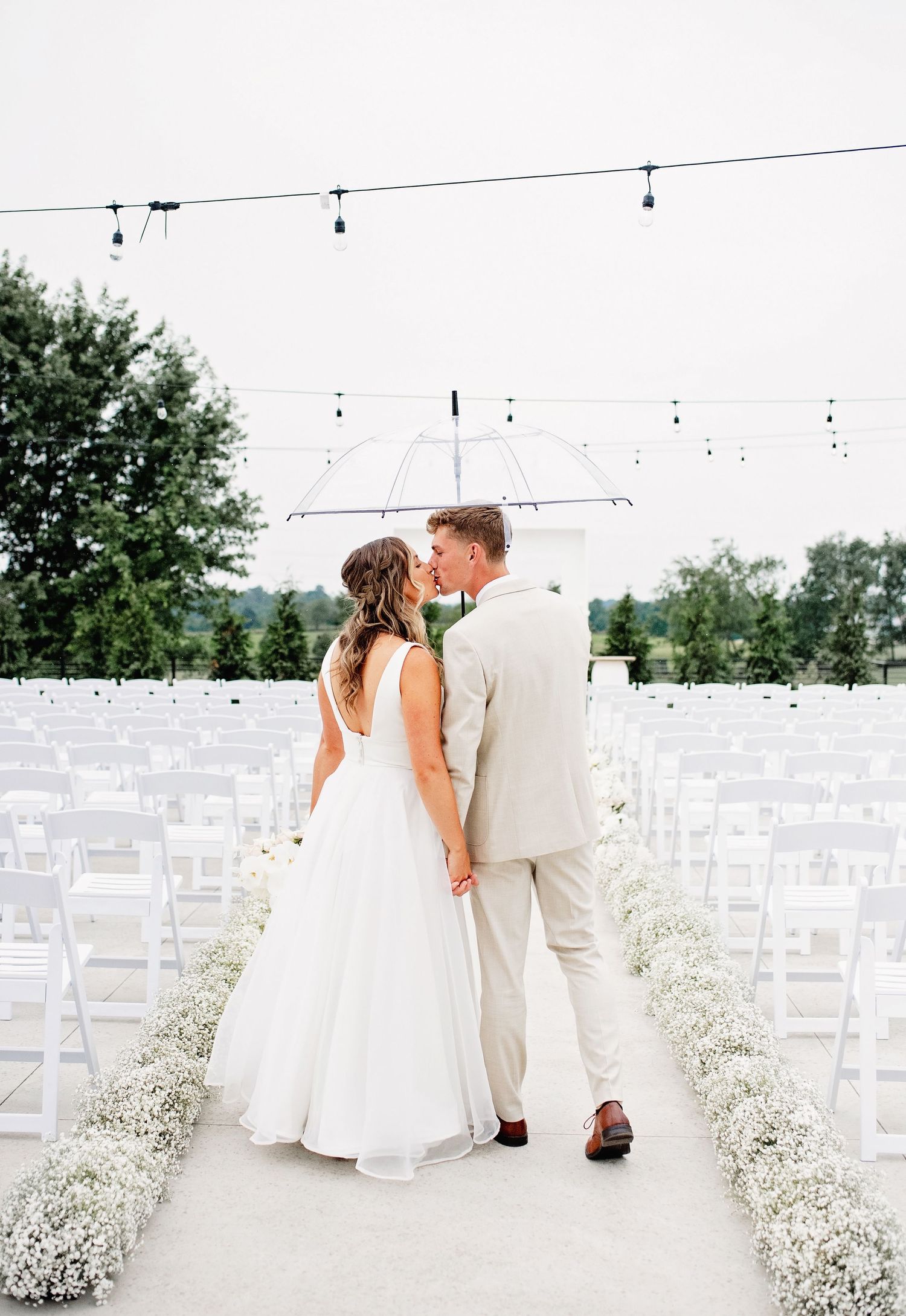 Wedding ceremony setup with string lights and baby's breath lined aisle.