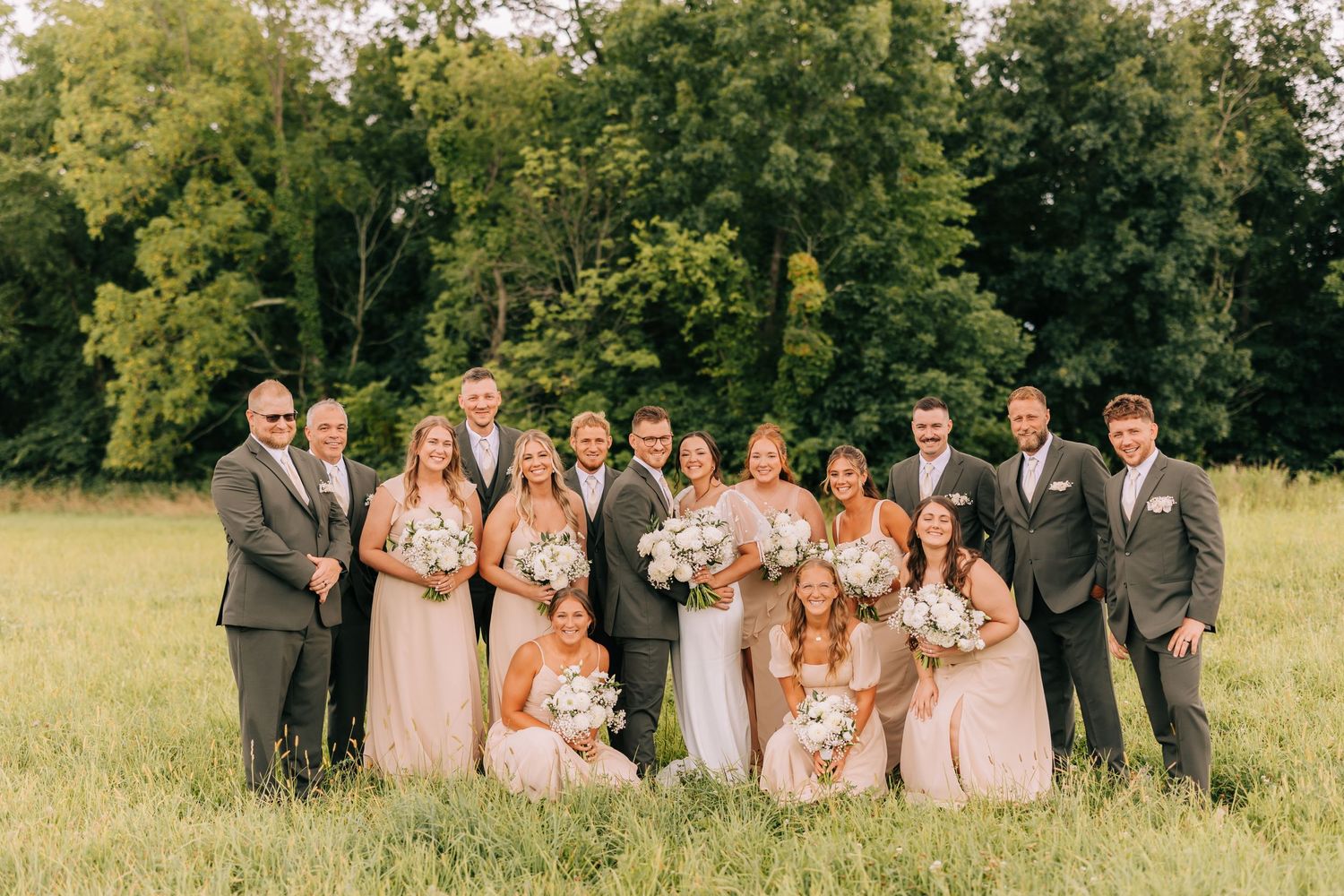 Wedding party in blush and gray attire poses together in a sunny field.
