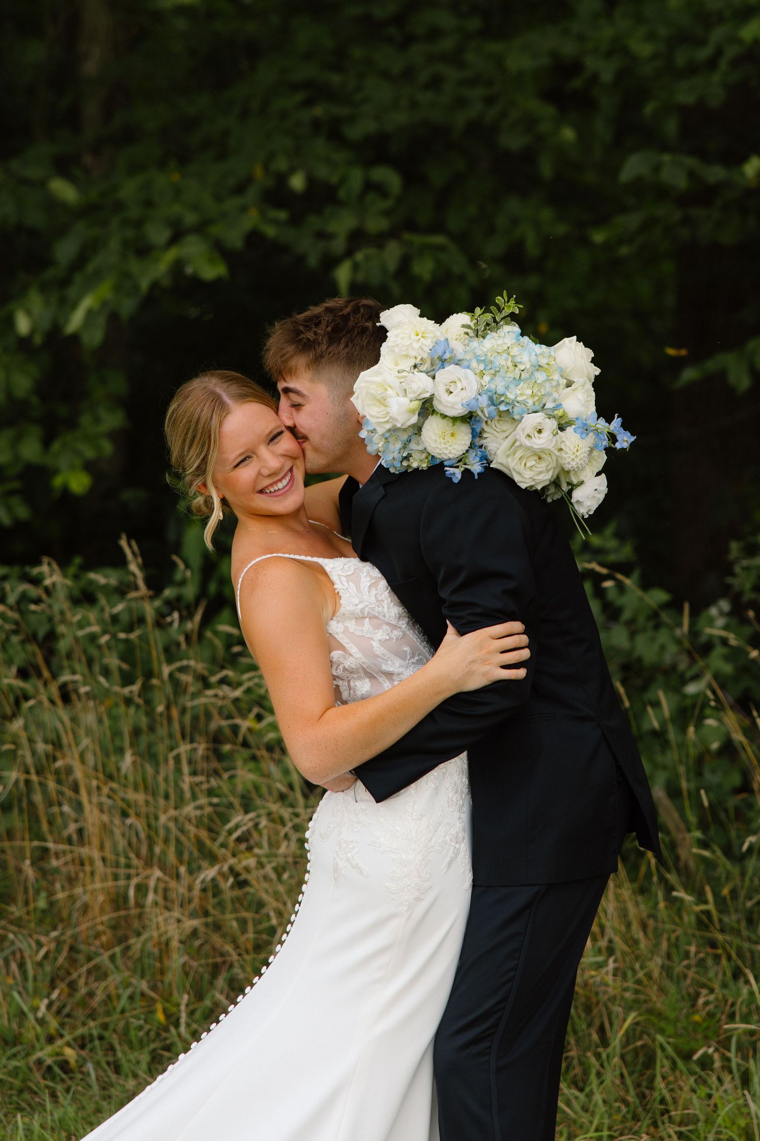 Romantic moment captured in a field with blue and white wedding bouquet.