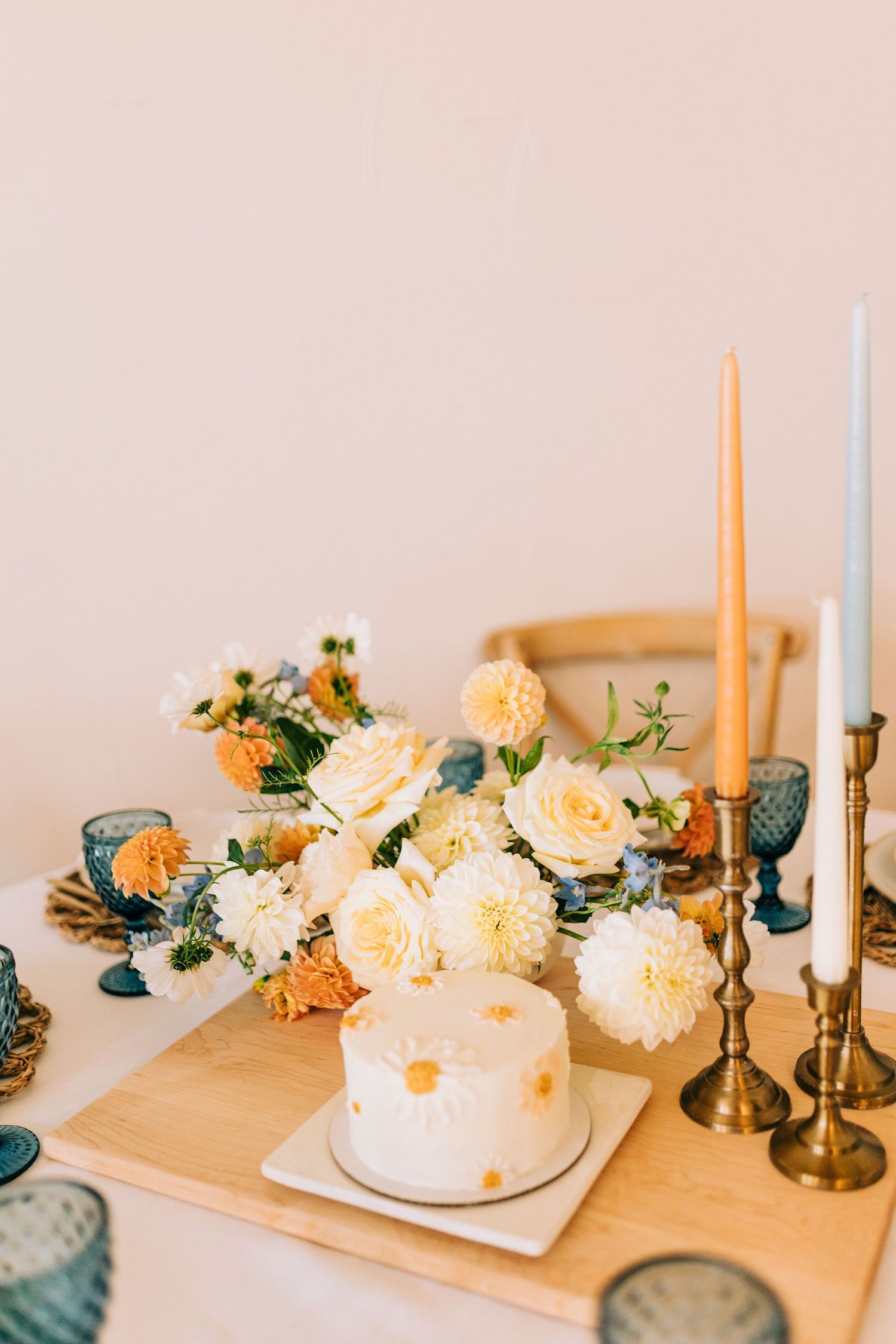 Wedding cake display with cream roses, blue glassware, and gold candlesticks on wooden table.