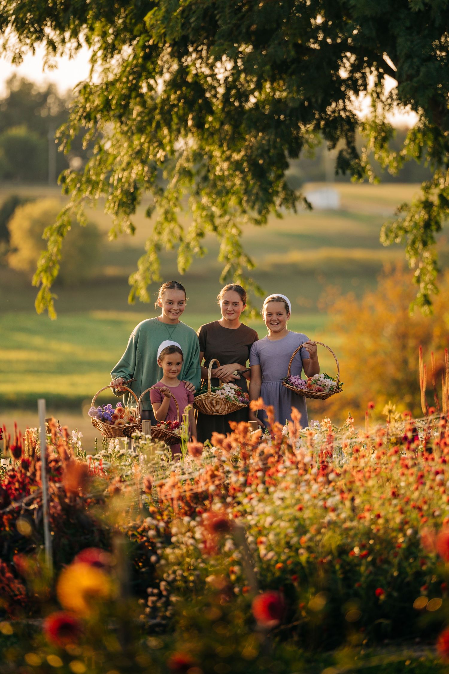 Group gathered in flower garden at sunset holding harvest baskets.