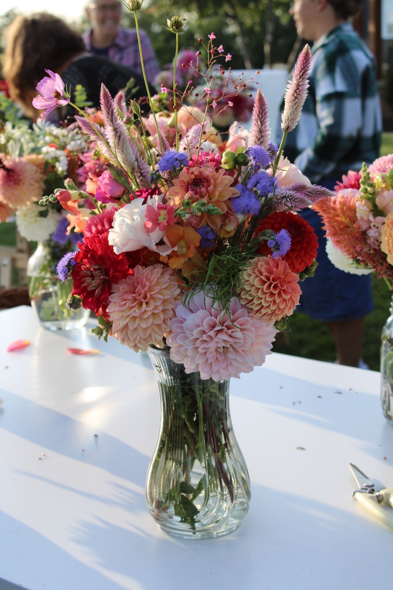 Stunning arrangement of pink, purple and white flowers in a glass vase on white tablecloth.