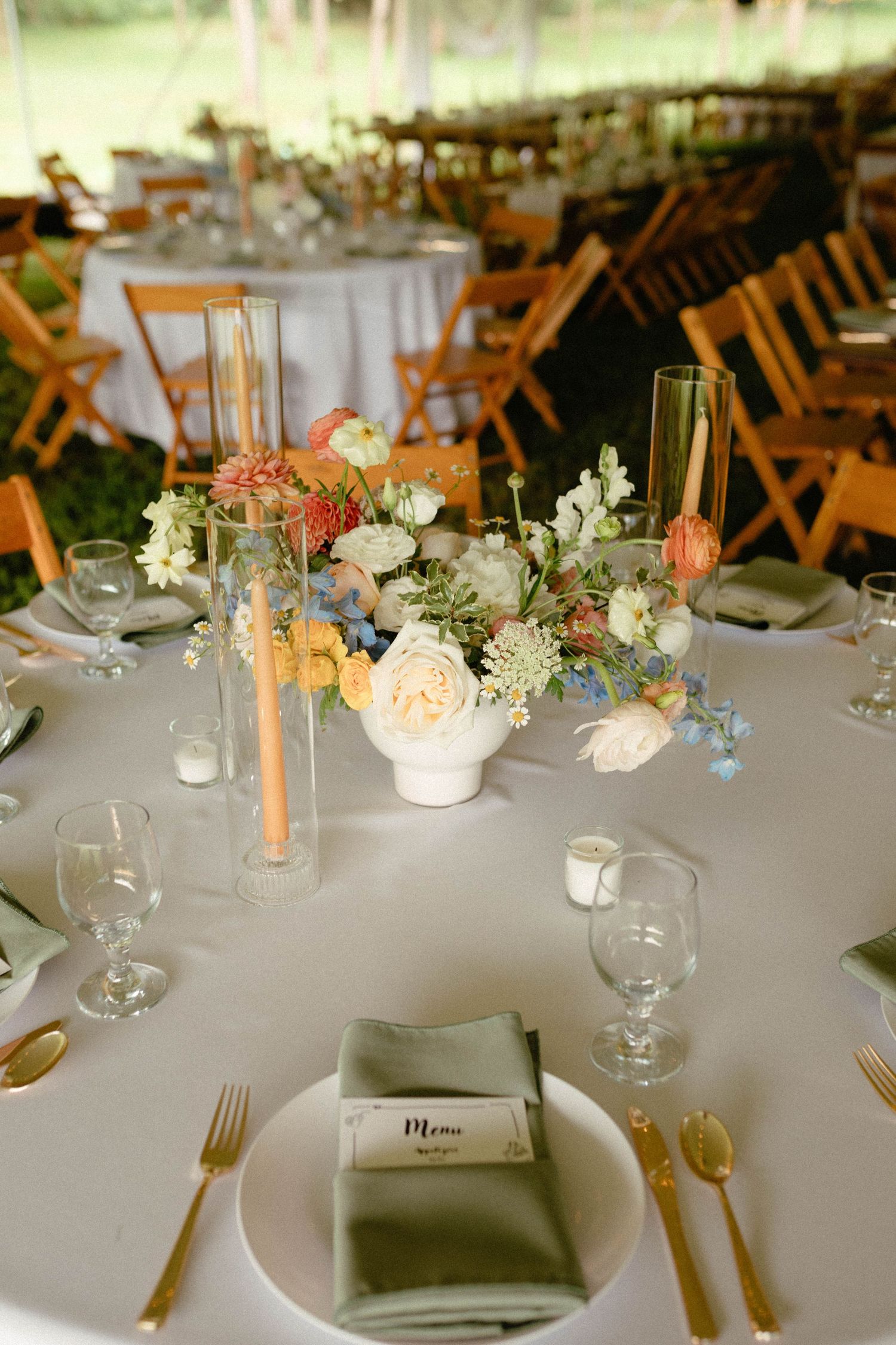 Elegant wedding reception table settings with white tablecloths, peach floral centerpieces, and gold flatware.