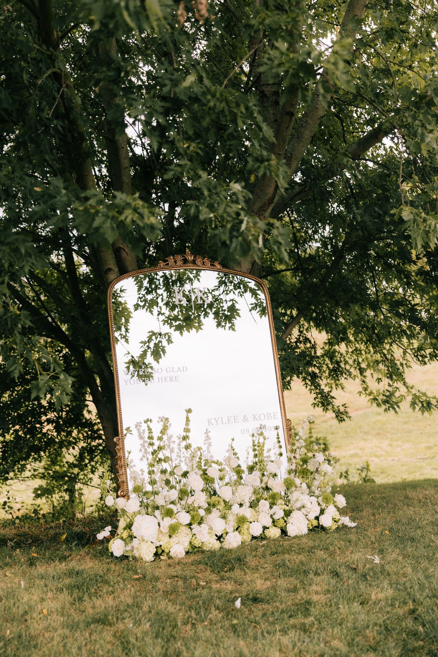 A white tent or canopy partially visible behind lush green trees and grass in an outdoor garden setting.