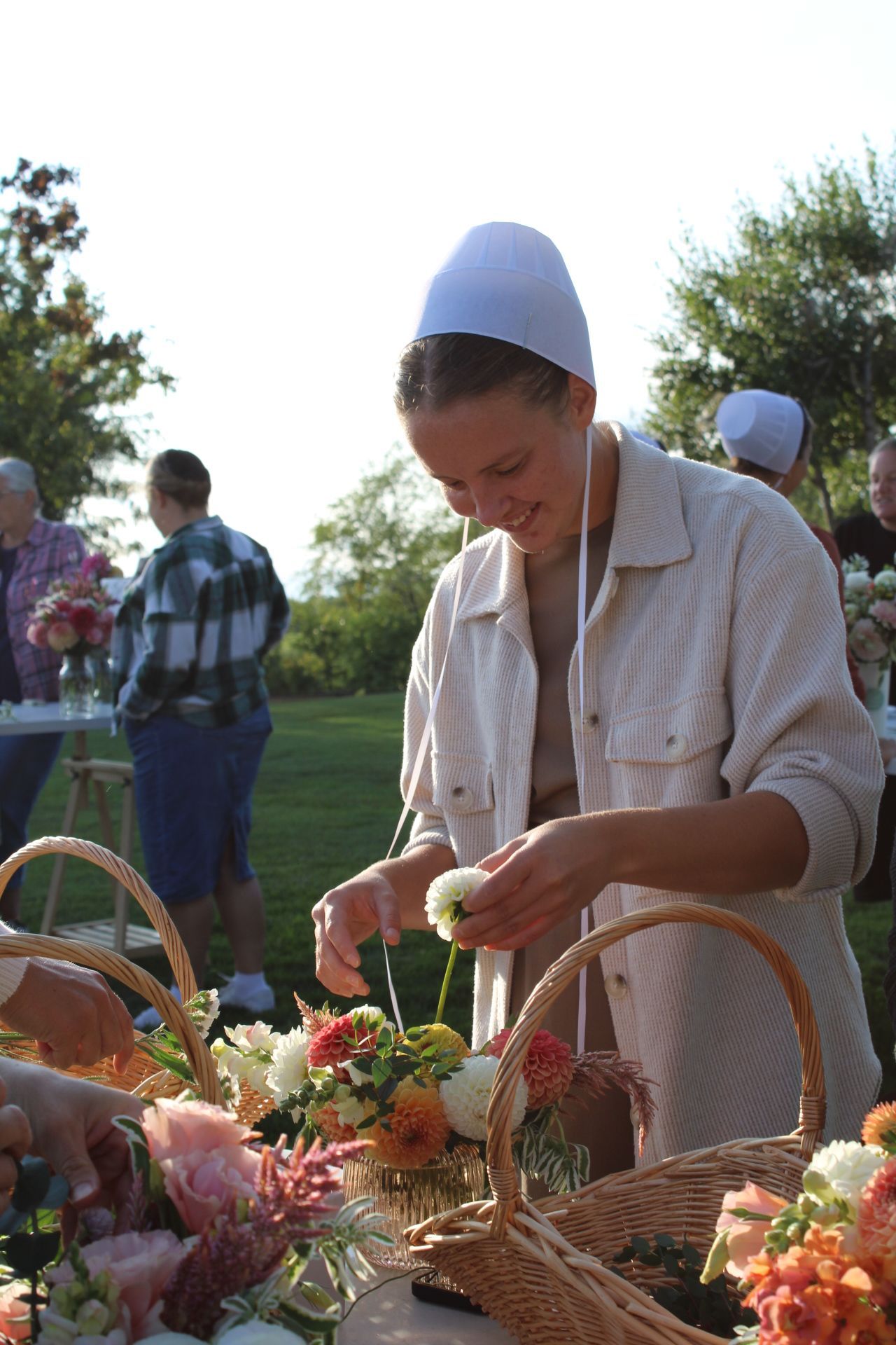 Person arranging flowers at an outdoor event with wicker baskets on table.
