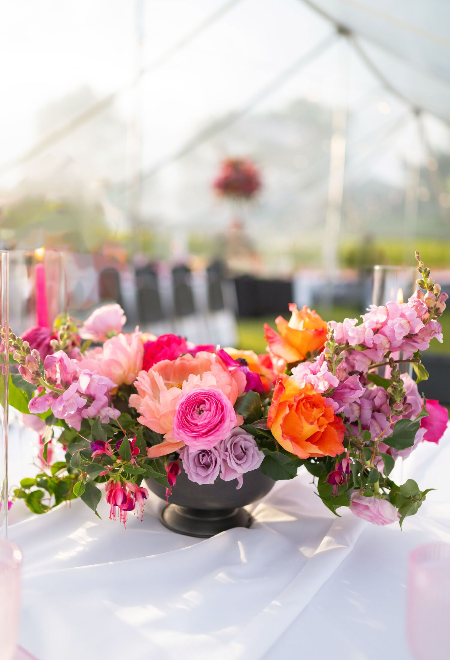 Colorful floral centerpiece with pink, orange and coral roses in a black vase on white tablecloth.