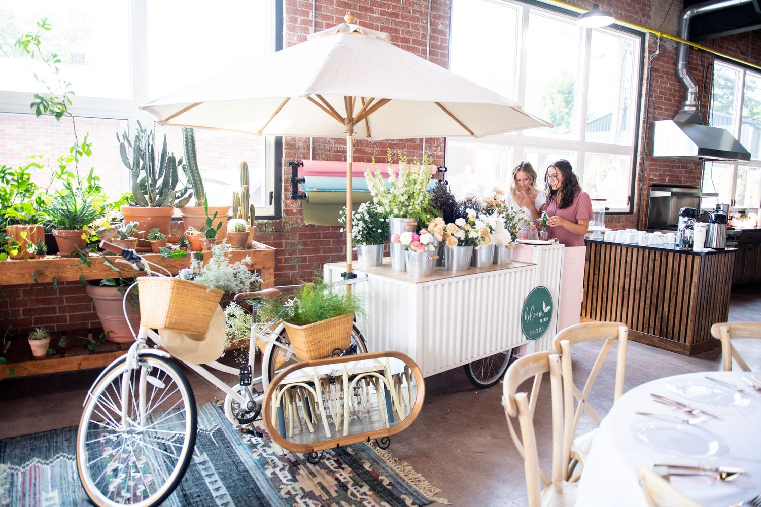 Vintage bicycle and floral cart setup at an indoor market with umbrella and decorative displays.