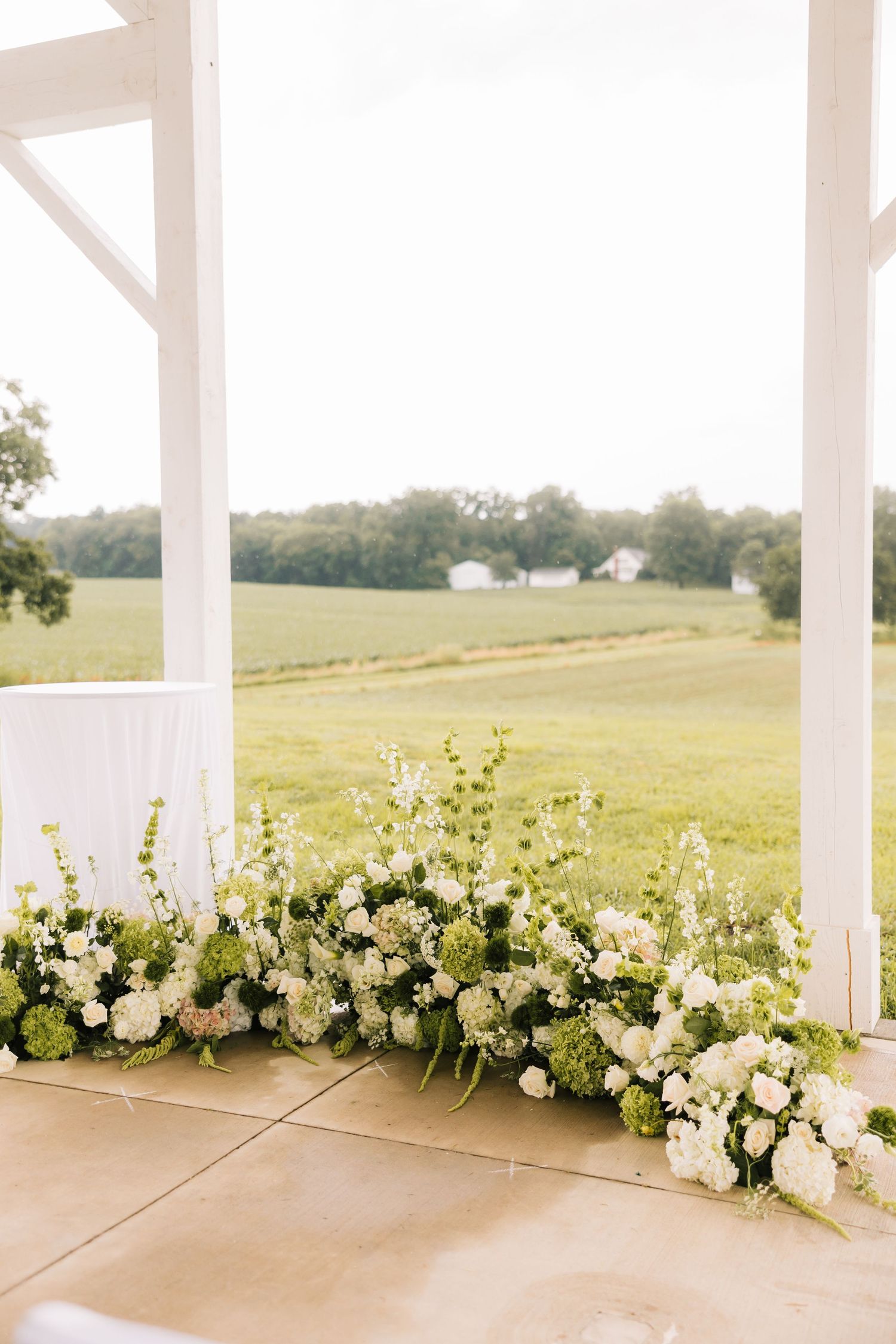 White floral arrangements line the edge of an outdoor patio overlooking a rolling green hillside landscape.