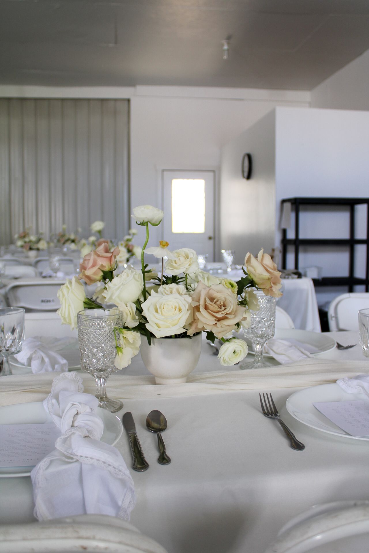 Romantic table settings with crystal glassware, white roses, and blush floral centerpieces on crisp white linens.