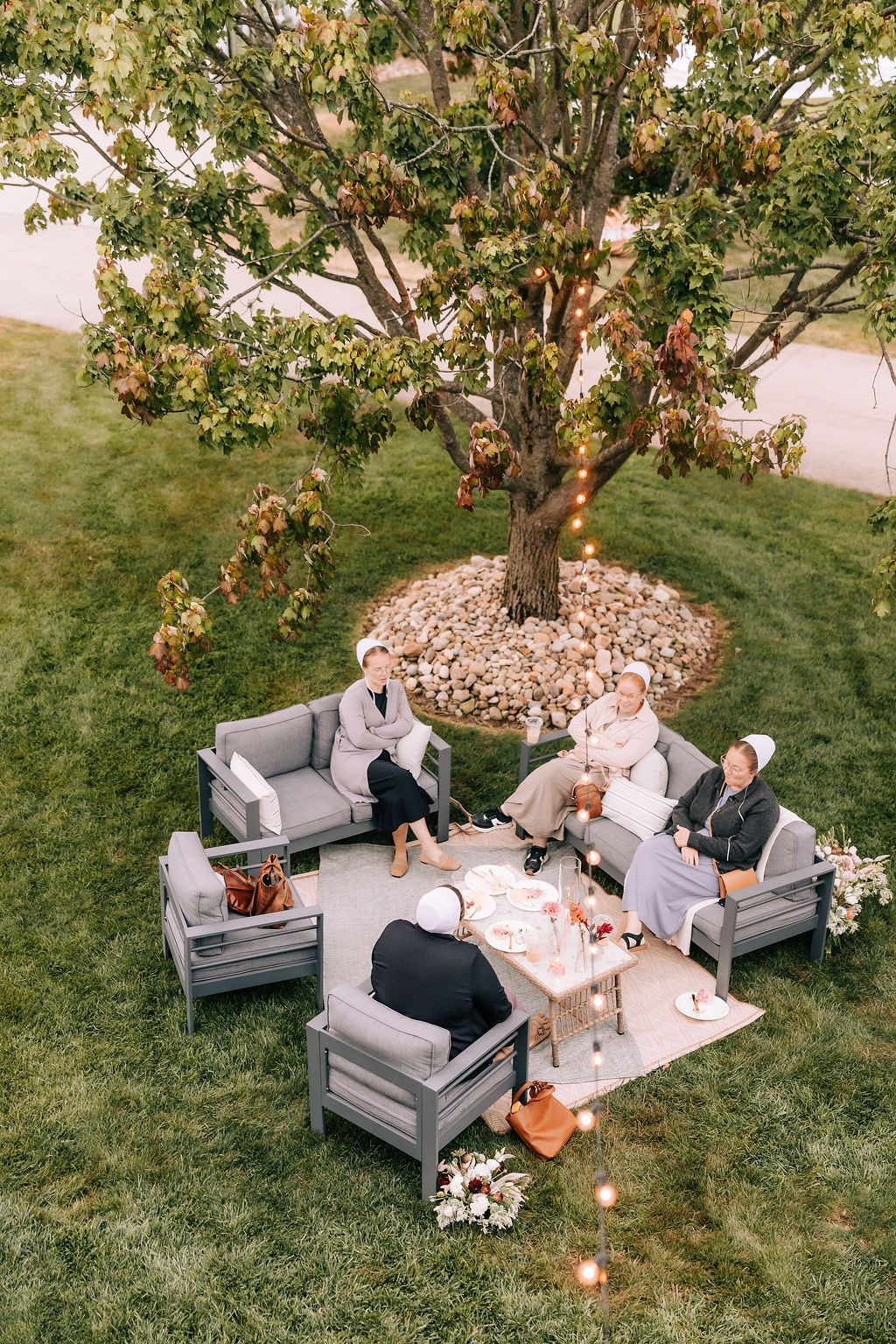 Cozy outdoor seating arrangement under a tree with romantic lighting and decorative pillows for an intimate gathering.