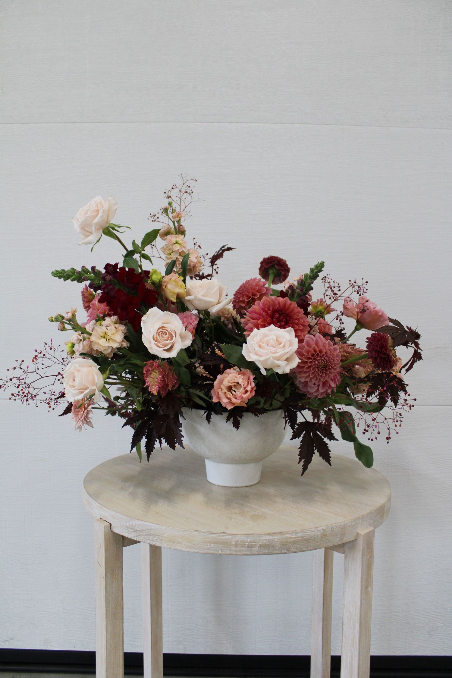 A luxurious floral arrangement with pink and burgundy blooms sits atop a round cream-colored pedestal table.