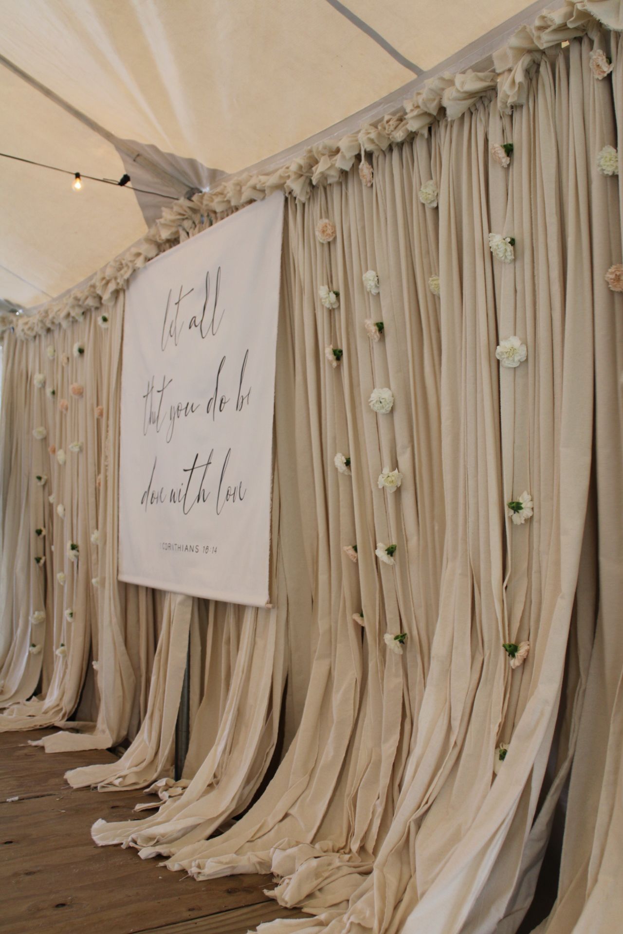 Romantic draped fabric backdrop with hanging flowers and inspirational quote sign for wedding ceremony.
