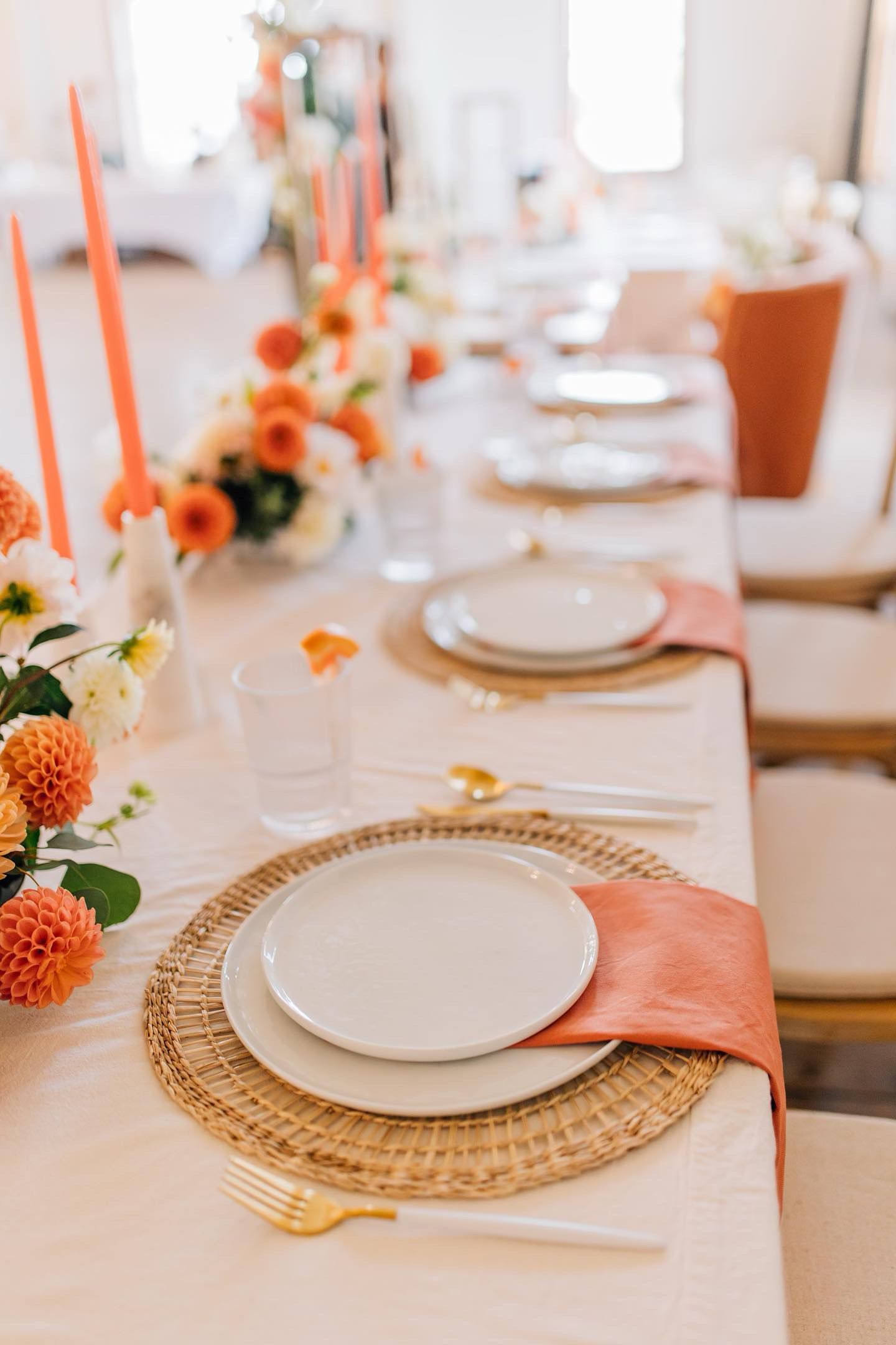 Table setting with woven charger, peach napkin, and coral floral centerpieces.