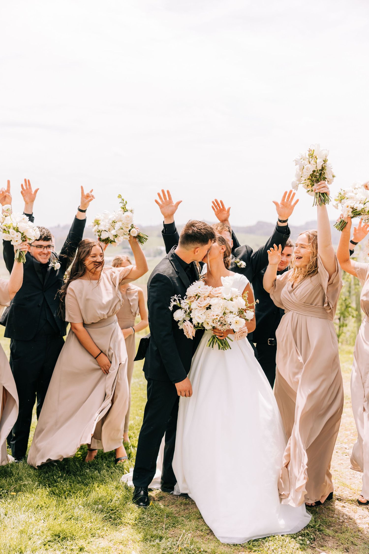 Wedding celebration with bridal party cheering outdoors in neutral colored attire.