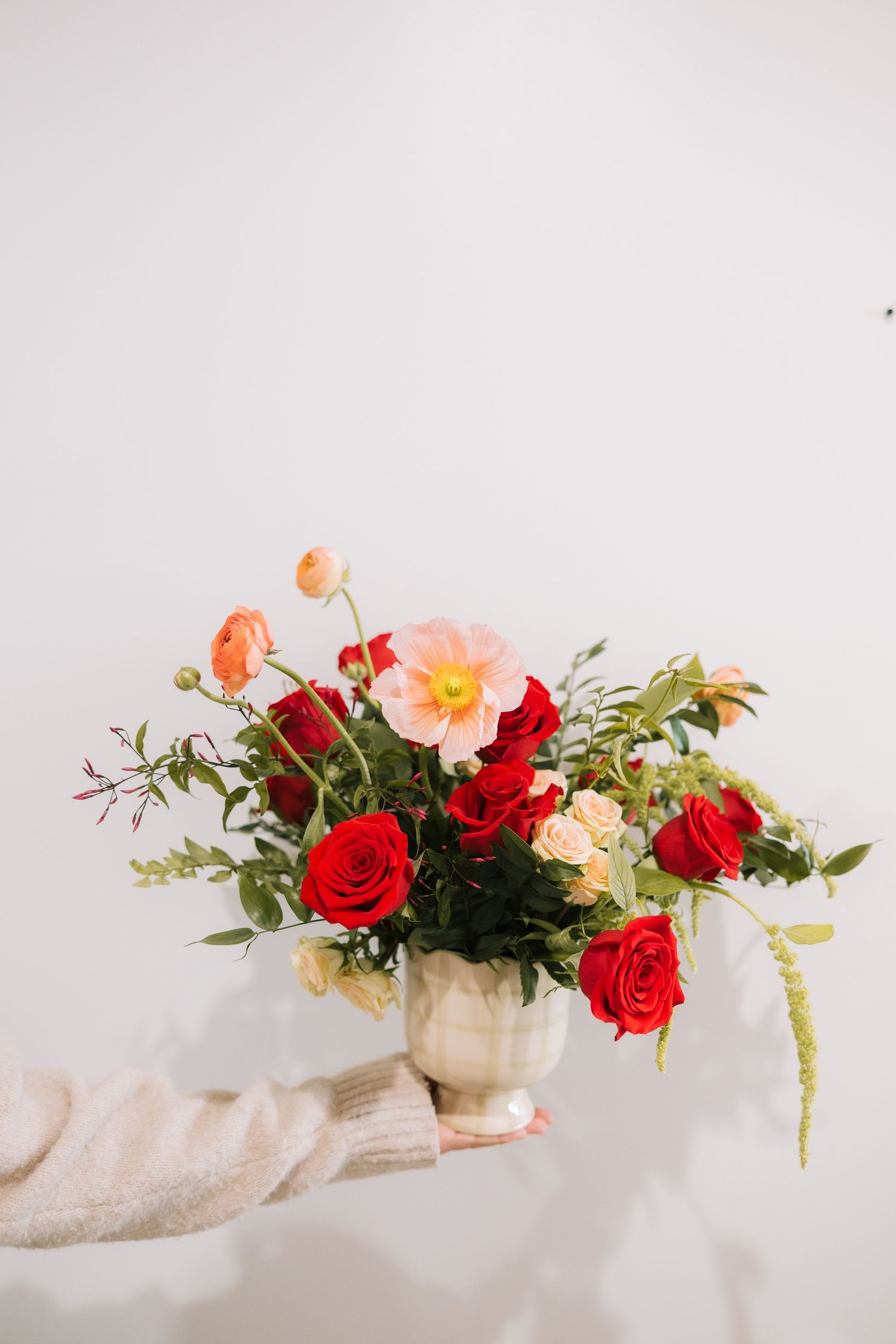 A romantic floral arrangement of red roses and peach blooms cascades across a light-colored fabric backdrop.