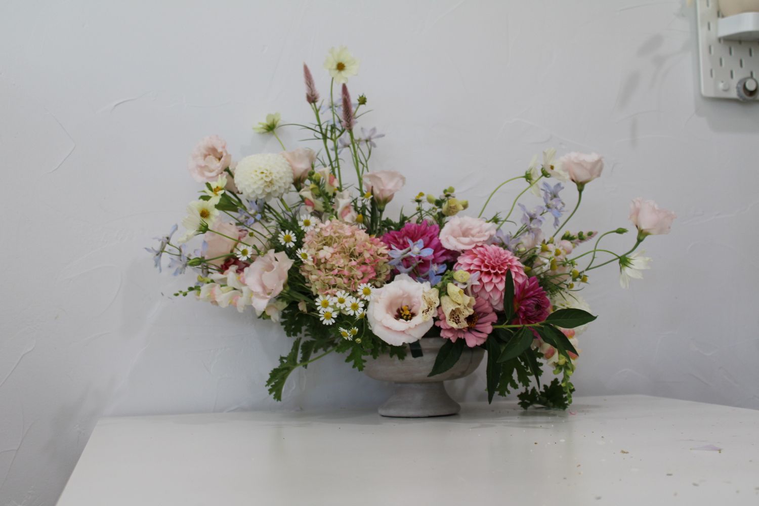 Soft pink and white floral arrangement with garden roses and delicate stems in a gray vessel.