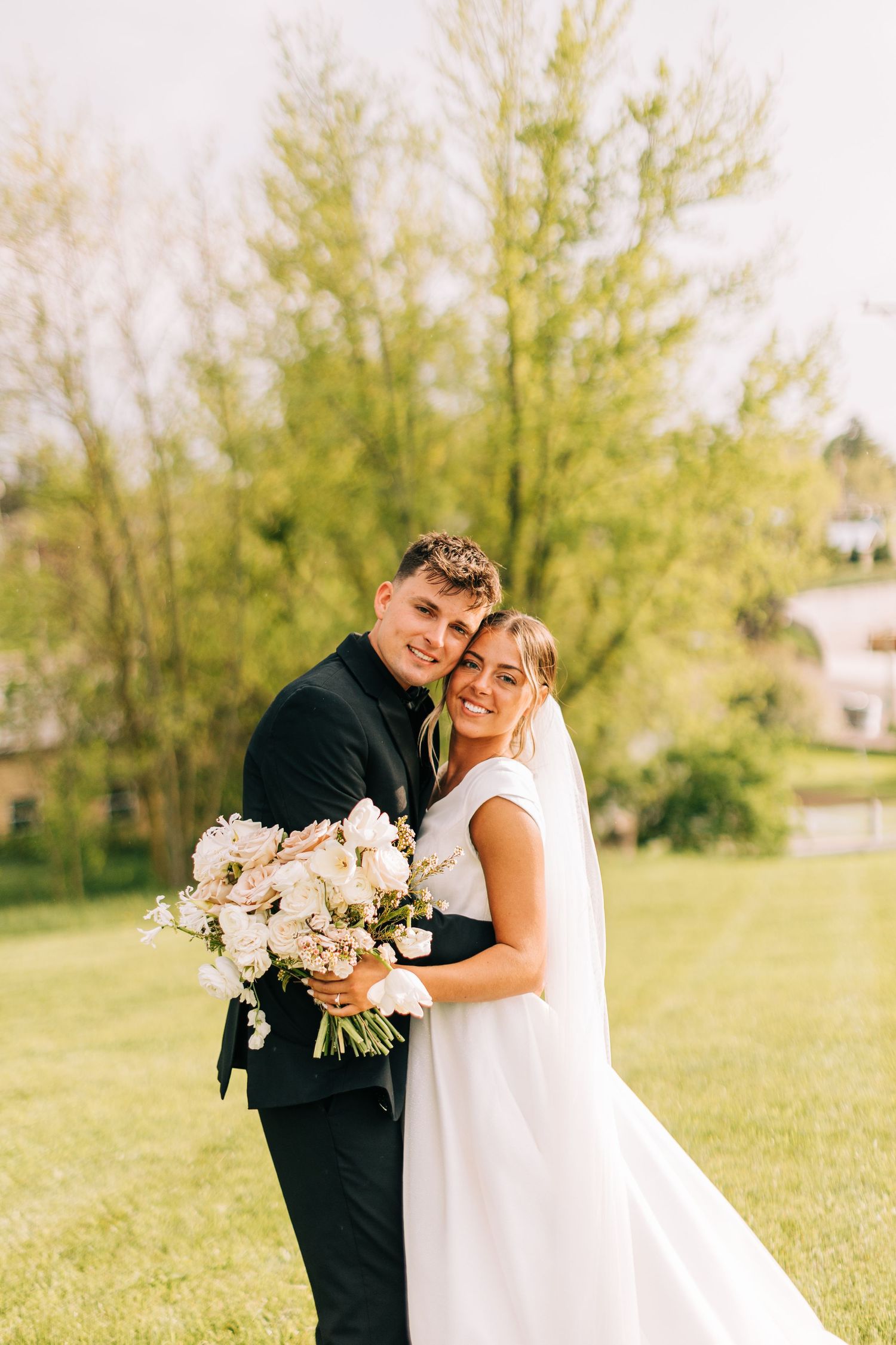 Outdoor wedding portrait featuring soft light and delicate bouquet against green landscape.