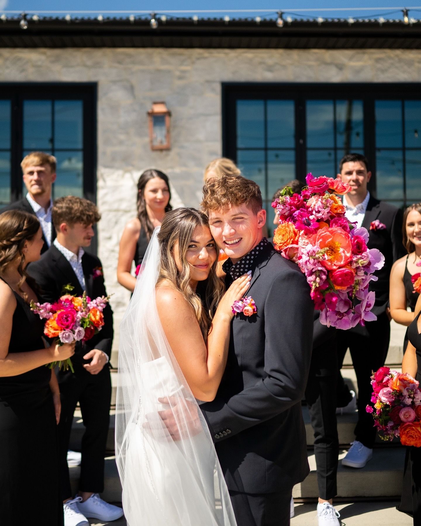Wedding celebration with bright floral arrangements outside modern architectural venue.