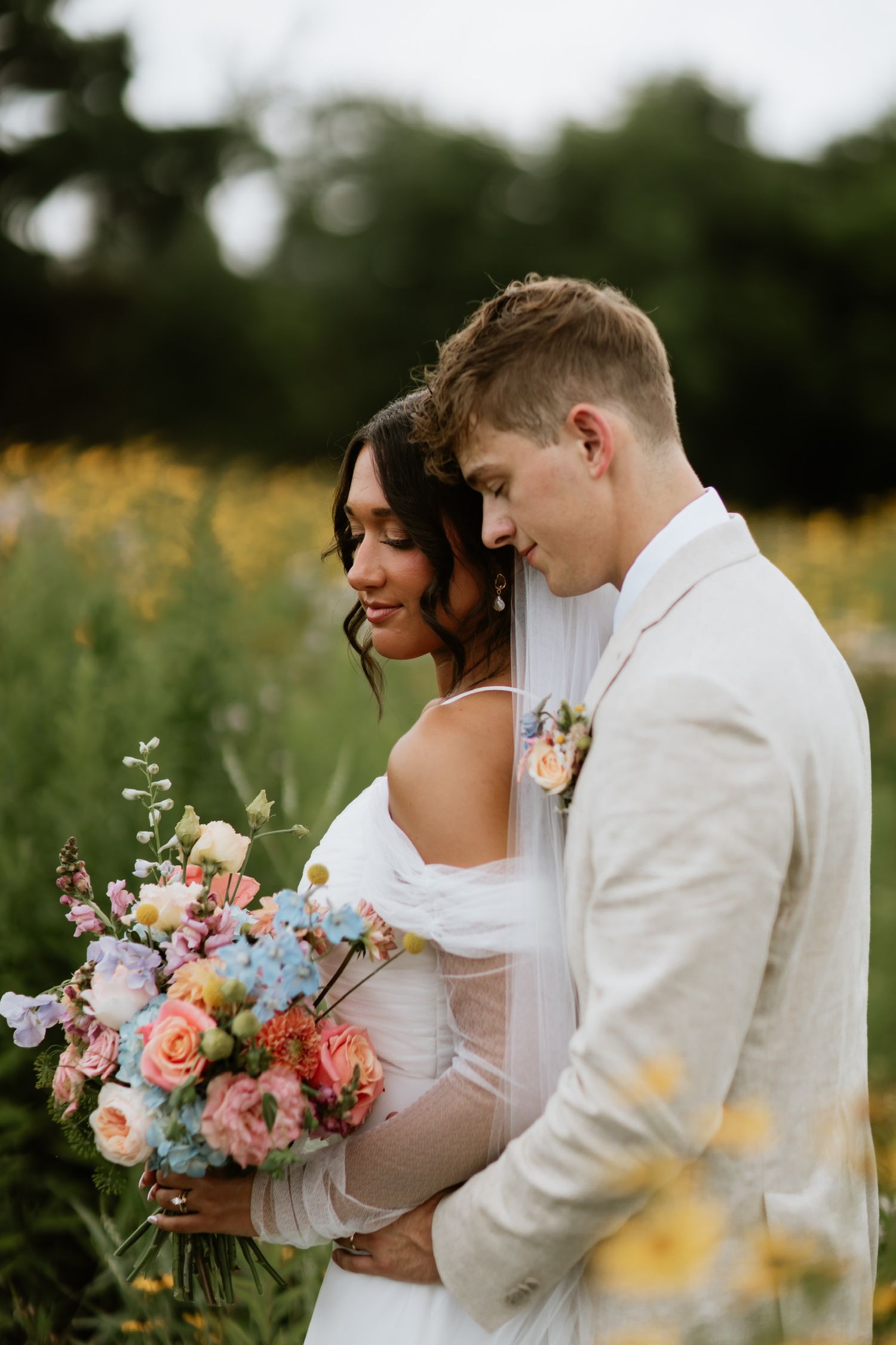 Intimate portrait of newlyweds with pastel bouquet in a wildflower field.