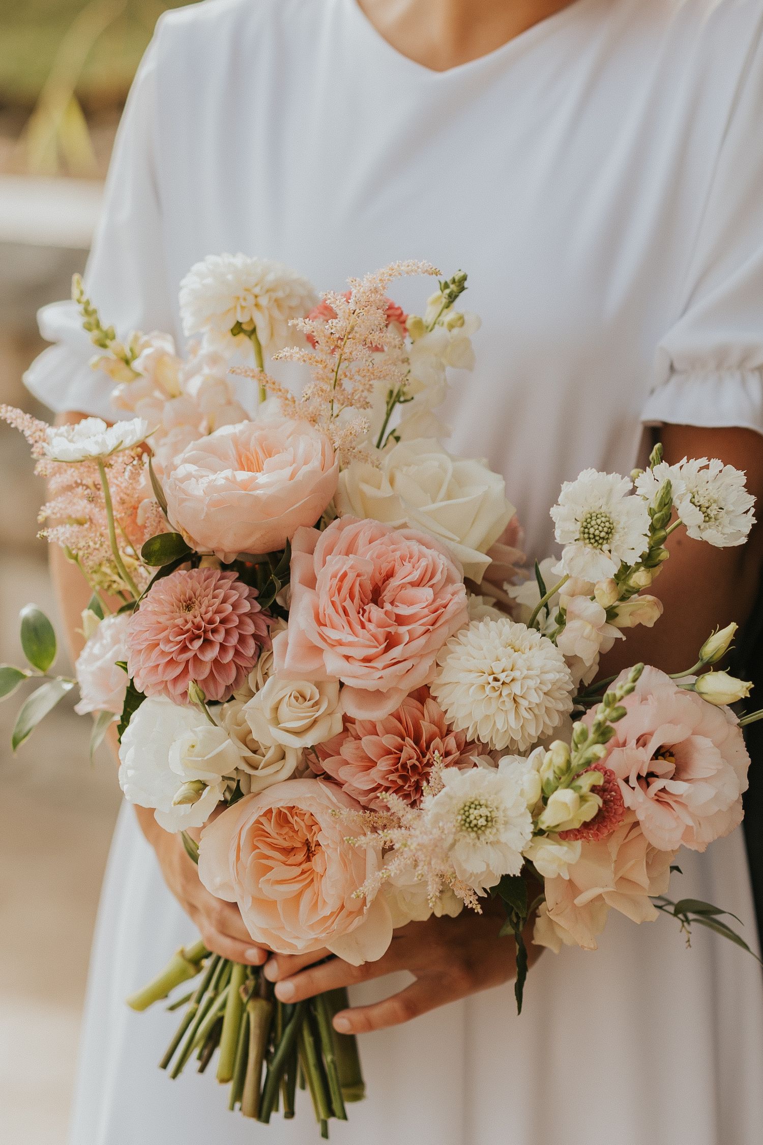Elegant bridal bouquet featuring soft pink dahlias, roses and white flowers arranged in a romantic garden style.