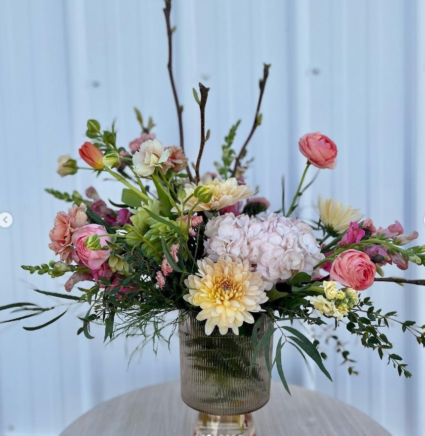 Garden-style arrangement with dahlias and roses in glass vase against blue background.