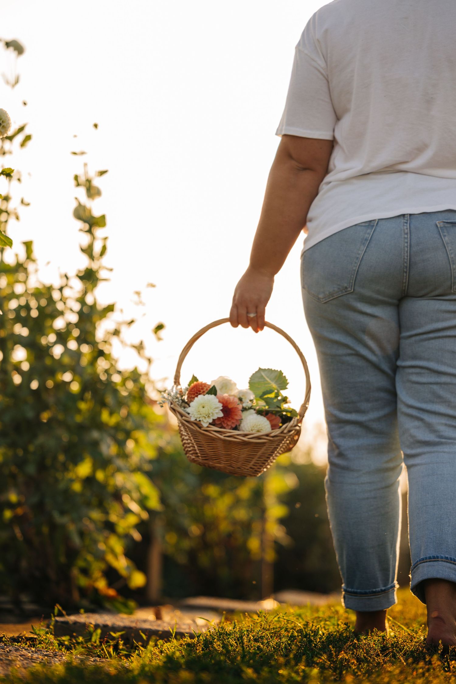 Person holding wicker basket with freshly picked flowers during golden hour.