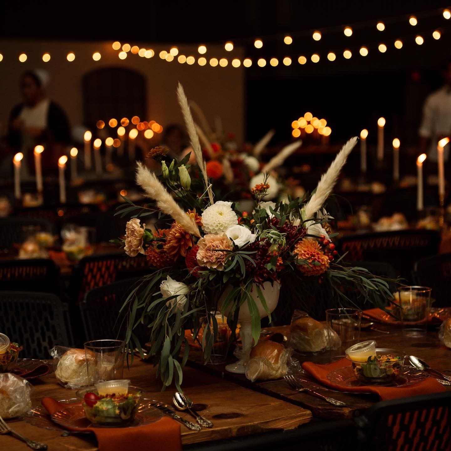 Elegant dinner table setting with moody lighting, floral centerpiece, and string lights creating a romantic atmosphere.