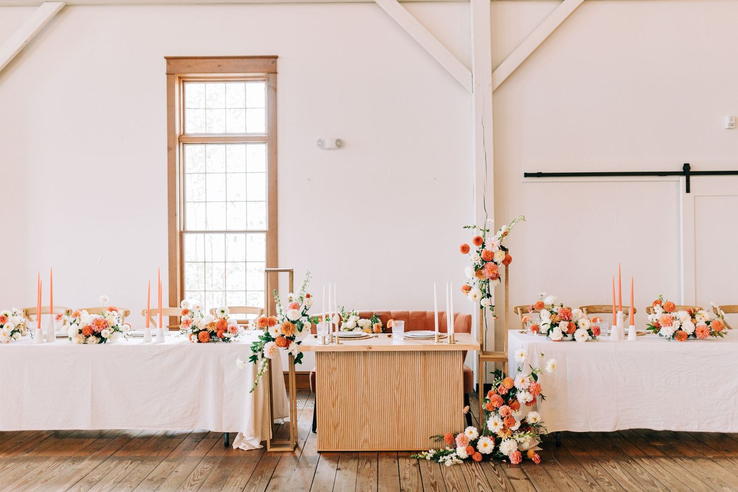 Wedding reception tables with white linens and peach floral arrangements in a bright rustic venue.