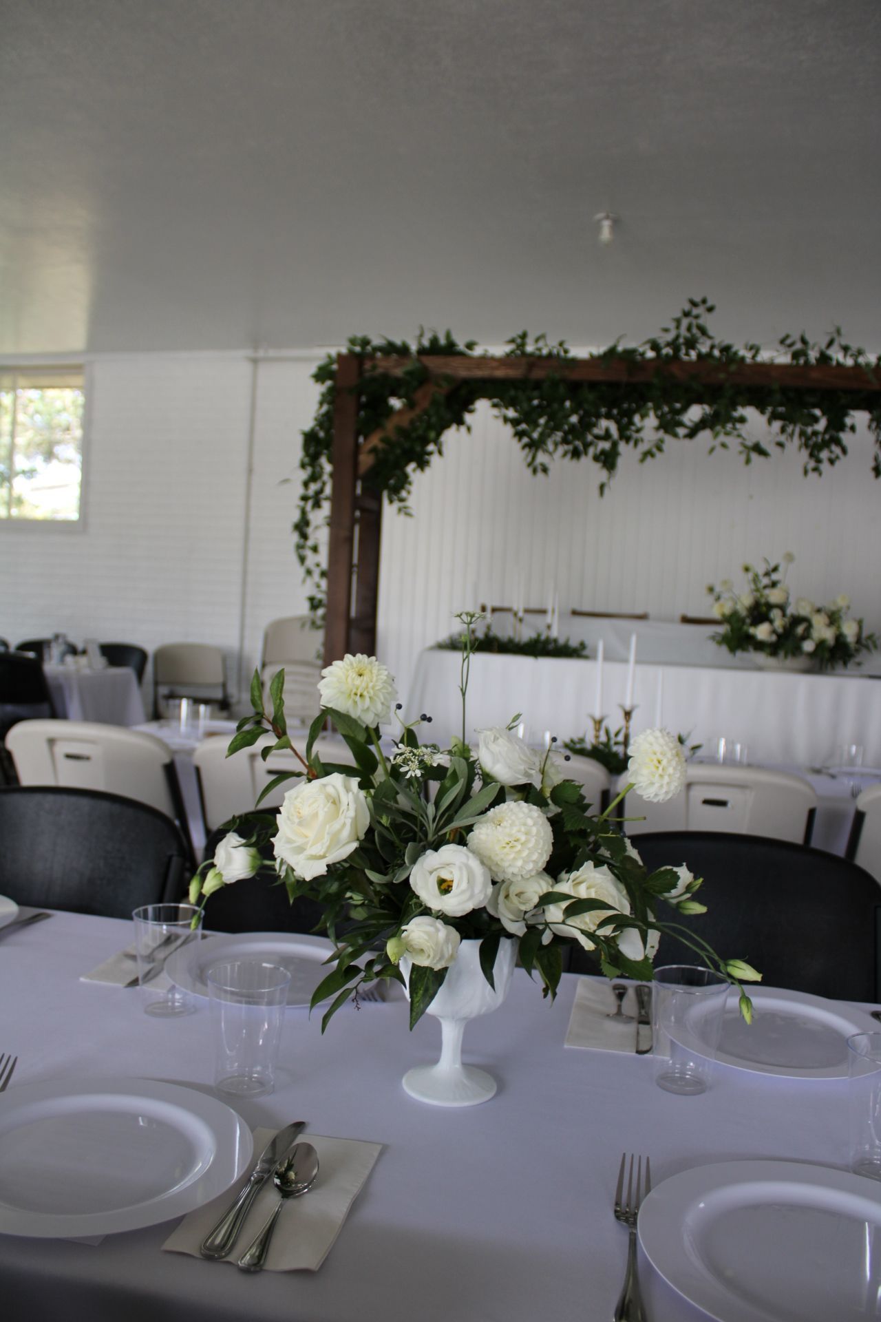 White and green floral centerpiece on round table with elegant place settings.