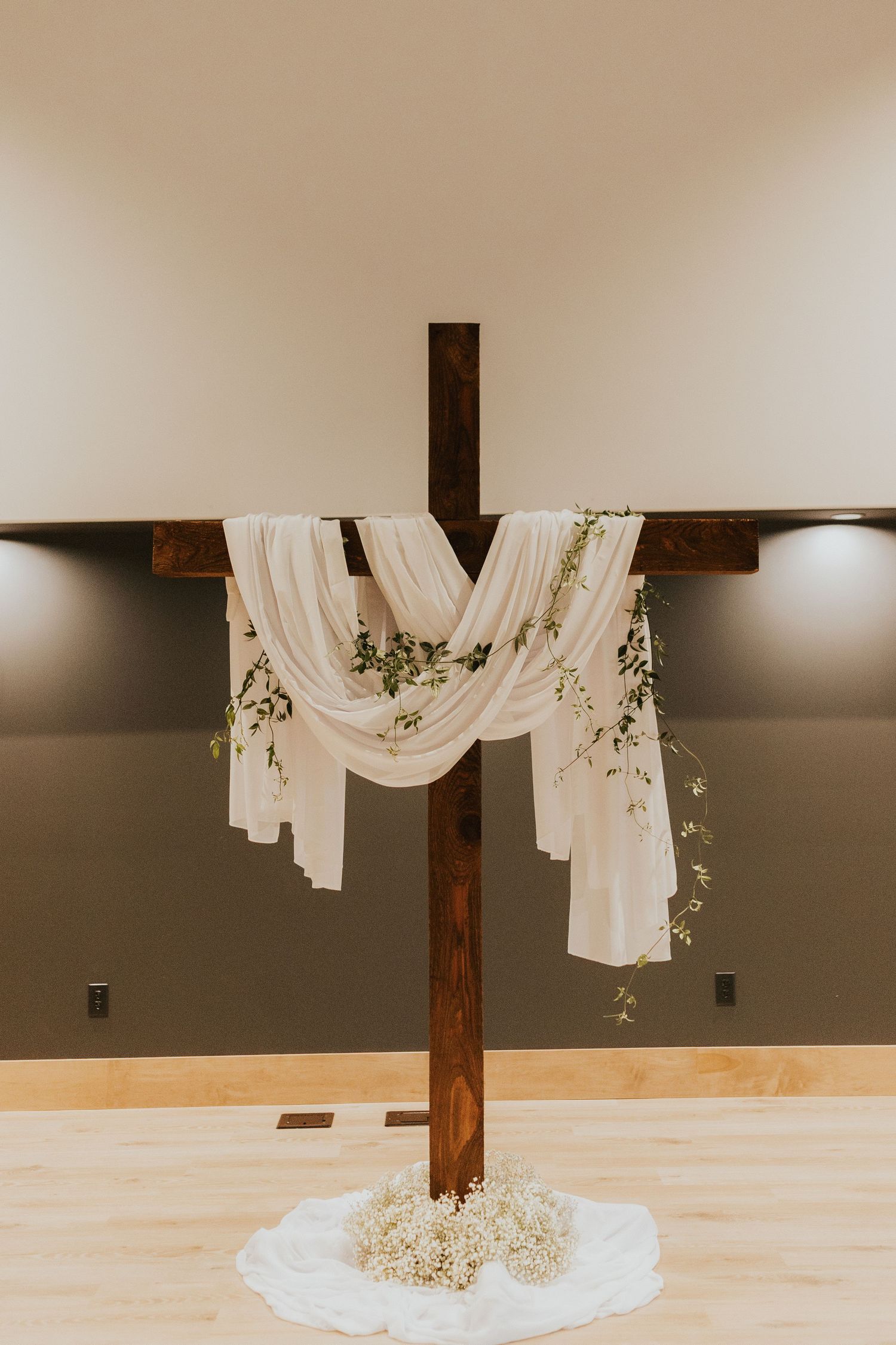 Rustic wooden cross beams draped with flowing white fabric and delicate baby's breath flowers create an elegant wedding altar.