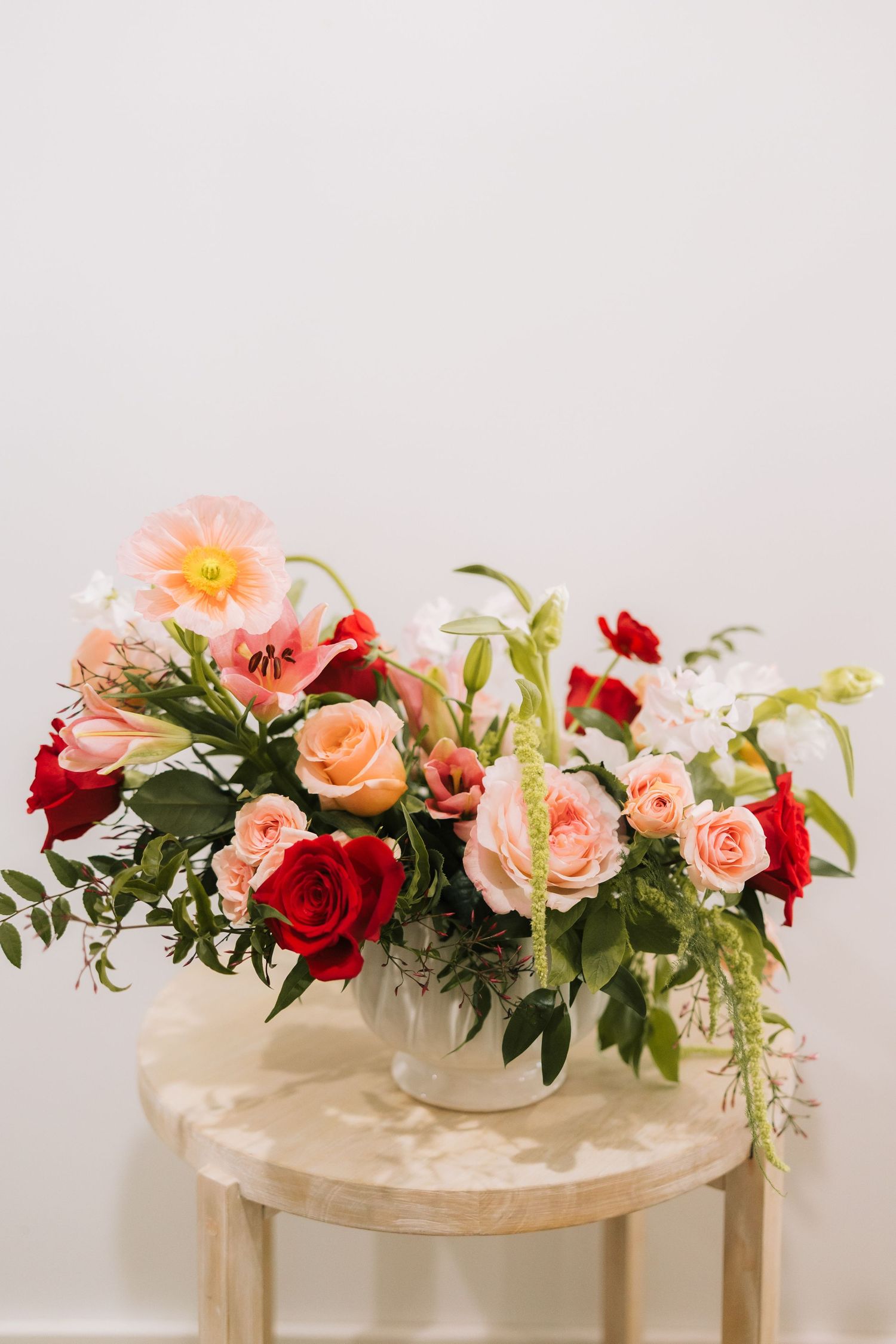 Elegant floral arrangement featuring pink and red roses with greenery displayed on a light wooden pedestal table.
