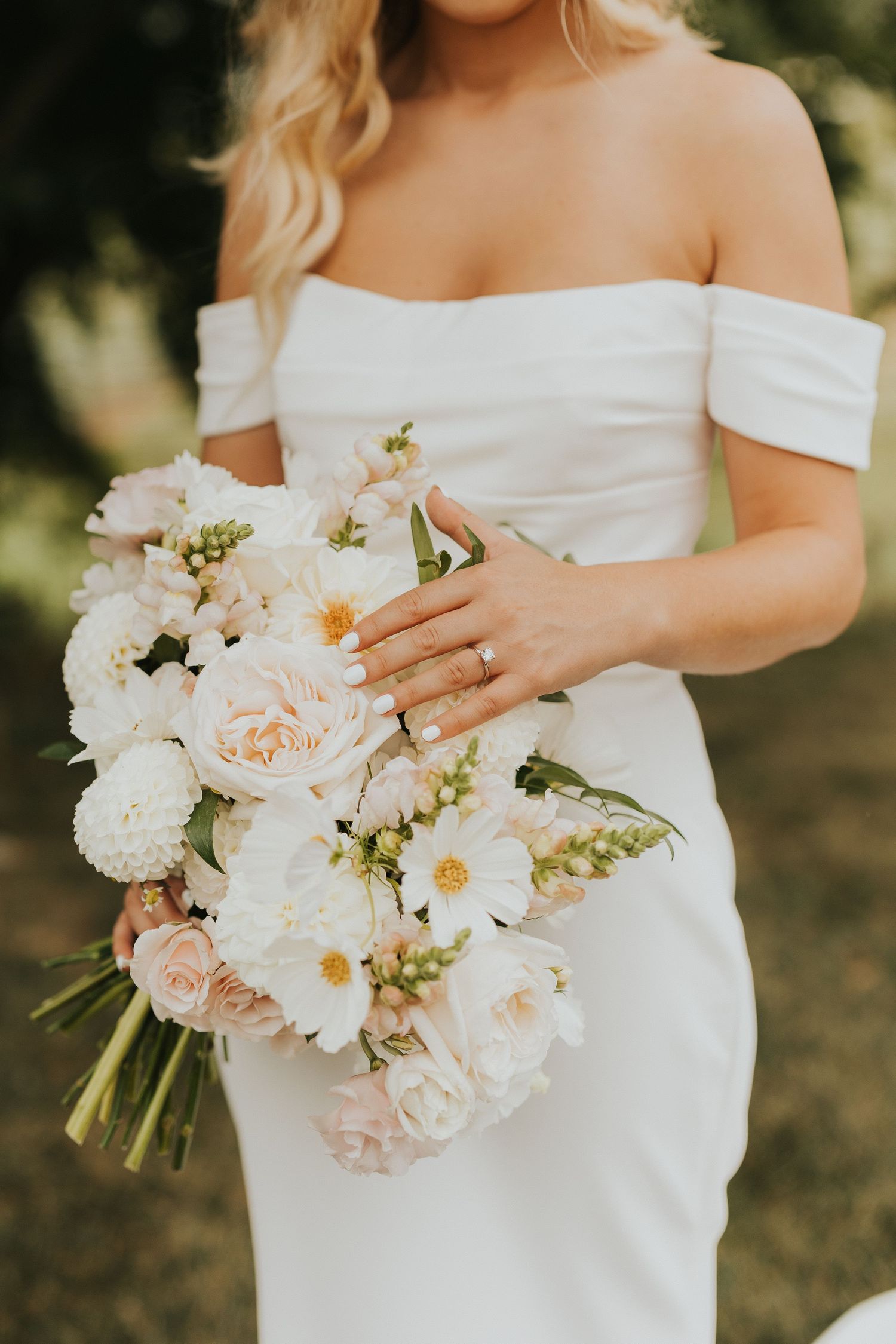 Close-up of a bridal bouquet with white and blush roses held against an off-shoulder wedding dress.