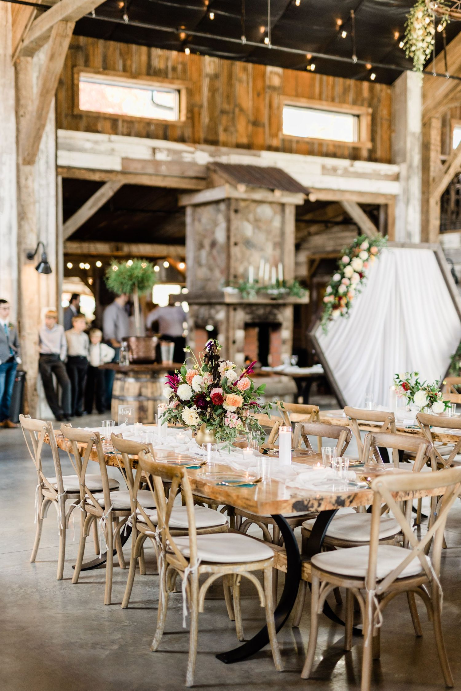 Rustic barn wedding reception with wooden crossback chairs and floral centerpieces.