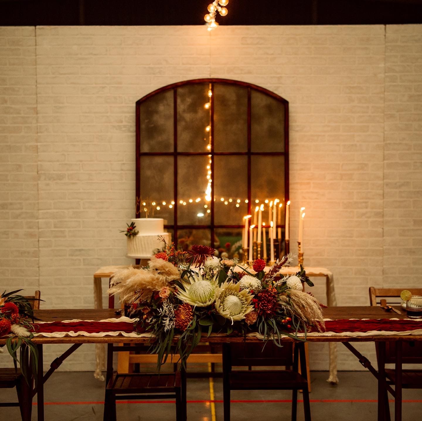 Moody reception table setting with tall candles and floral arrangements against brick wall.