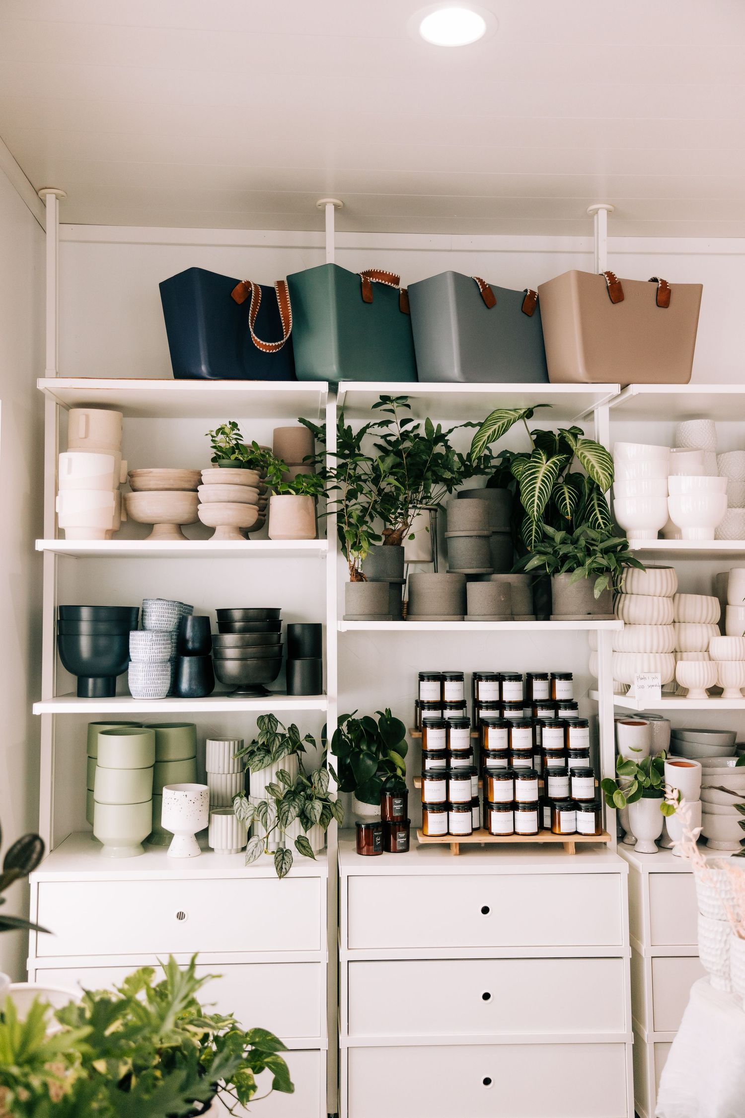 Well-organized retail shelving display featuring pottery, planters, tote bags and decorative items arranged on white shelves.