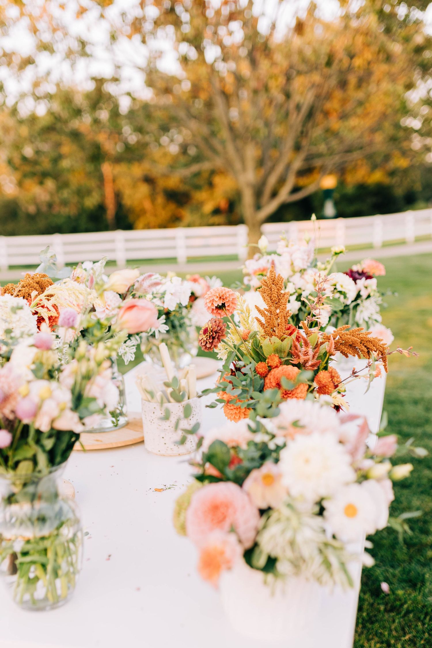 Beautiful floral arrangements with pink and peach blooms displayed on white tables in an autumn garden.