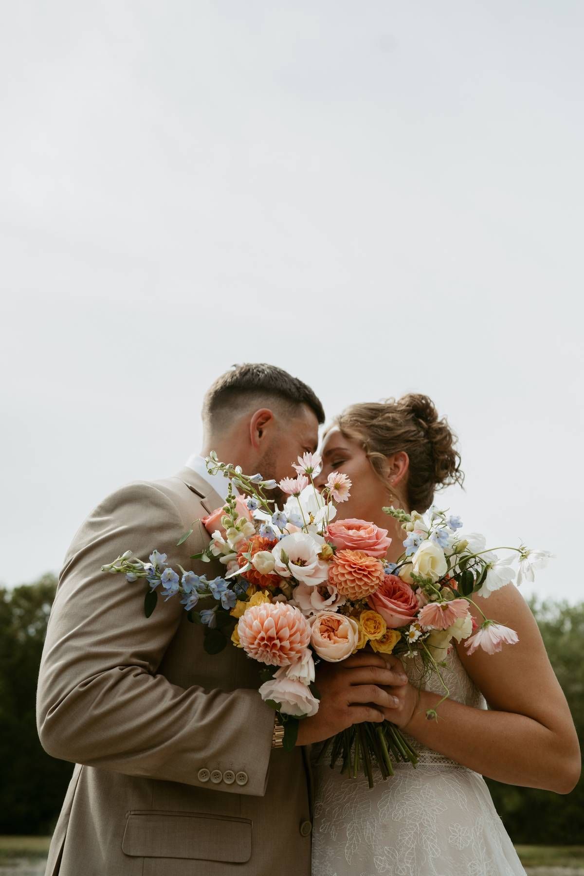 A romantic wedding couple shares a tender moment while holding a beautiful peach and blue floral bouquet.