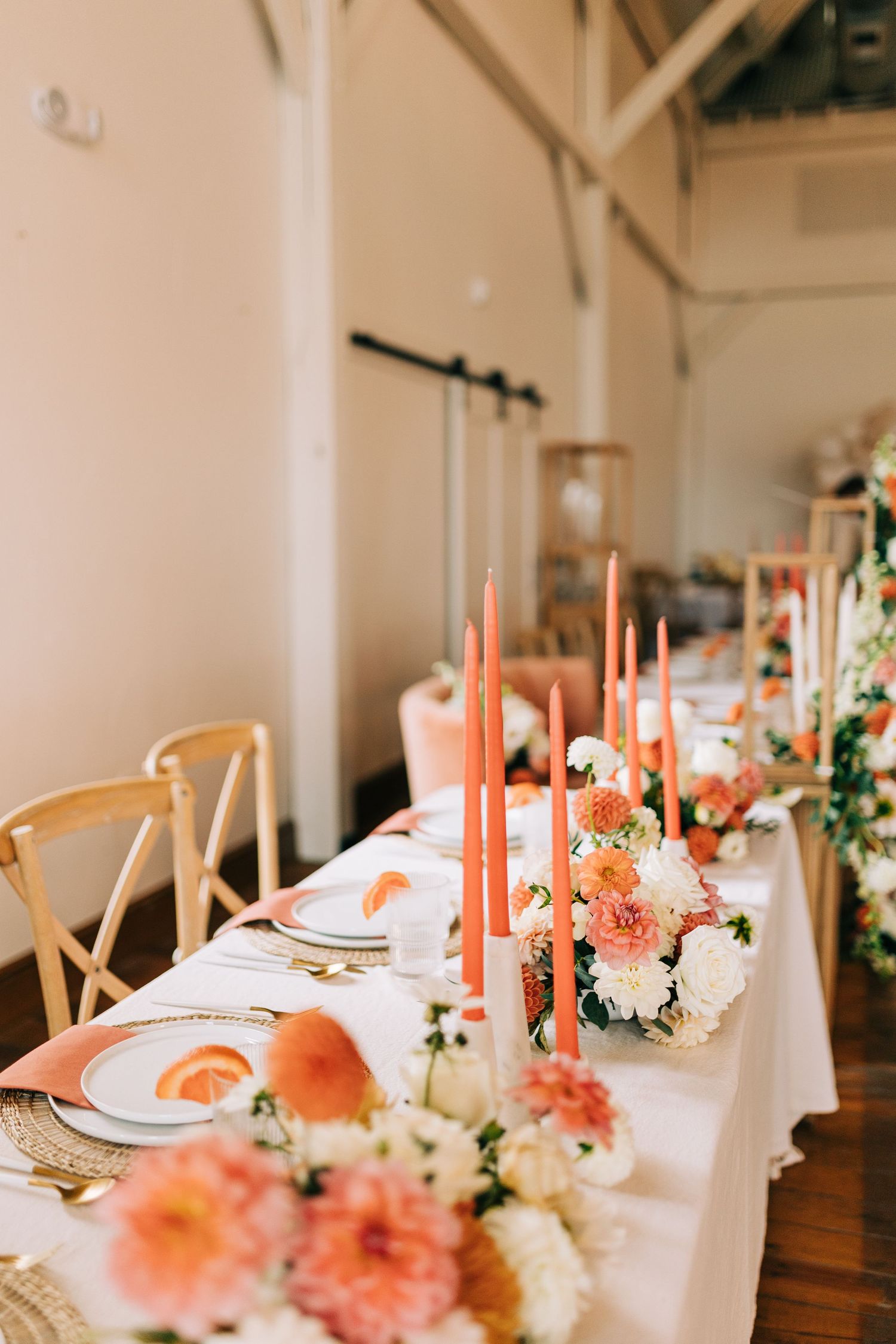 Elegant table setting with coral taper candles and peach floral arrangements on white linens.