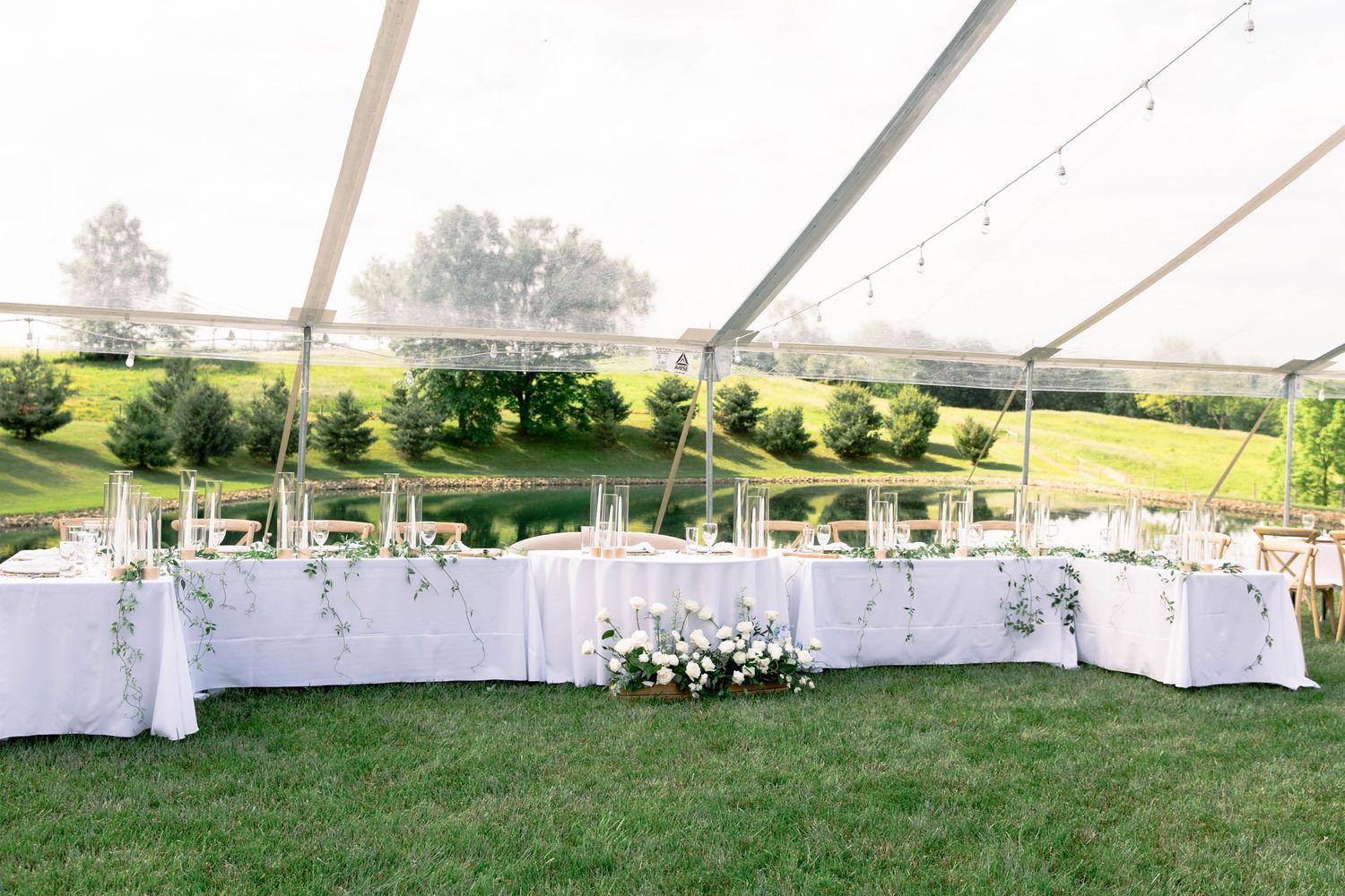 Outdoor wedding reception setup with white tables and chairs overlooking green countryside.