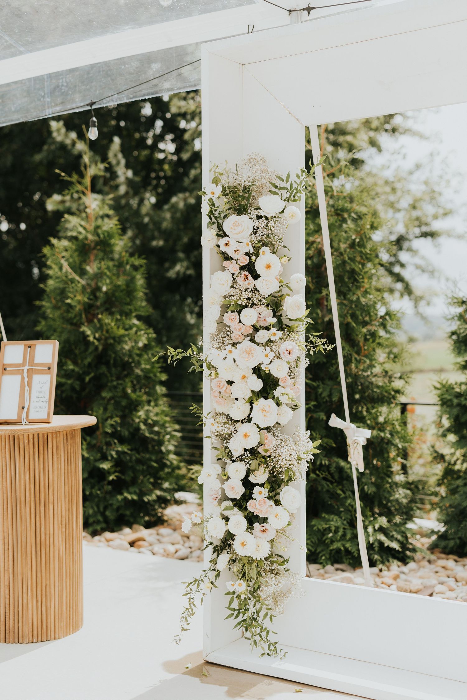 White wedding ceremony arch decorated with cascading white floral arrangements and greenery.