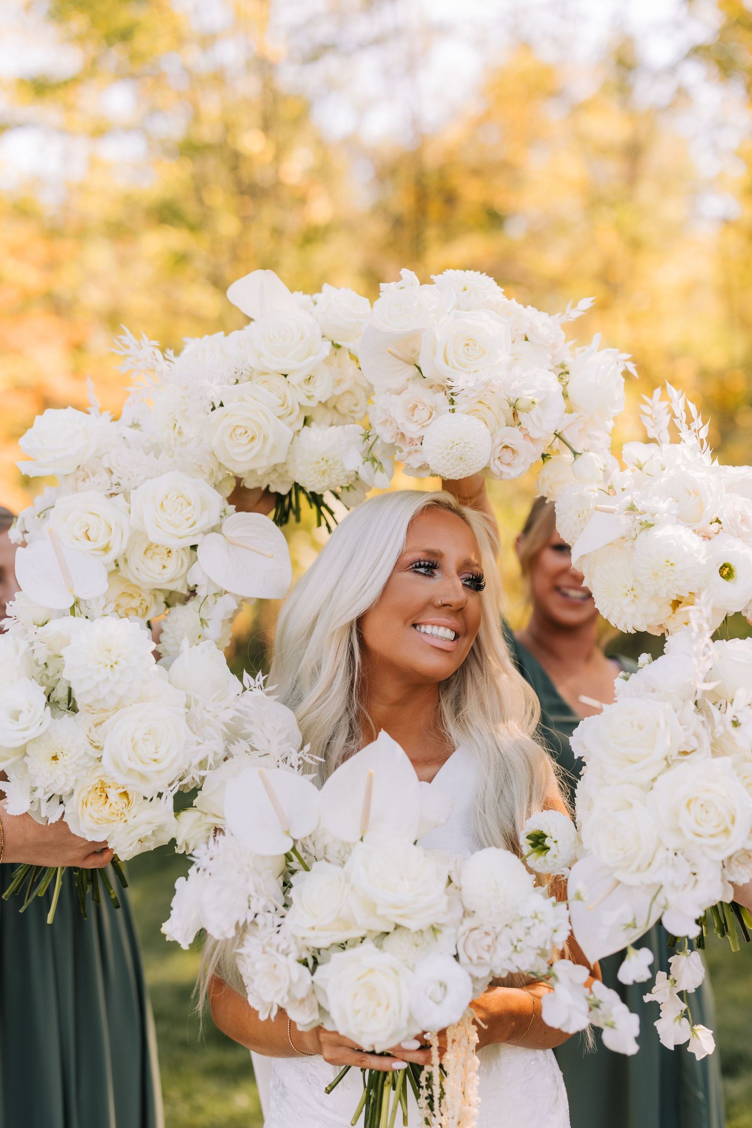 A row of elegant white orchid and rose bouquets held against emerald green dresses in natural sunlight.